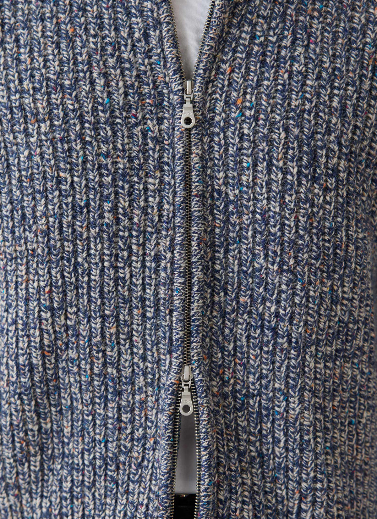 A close-up of the Percival Norton blue fleck zip cardigan, highlighting the chunky ribbed knit and double zip closure.