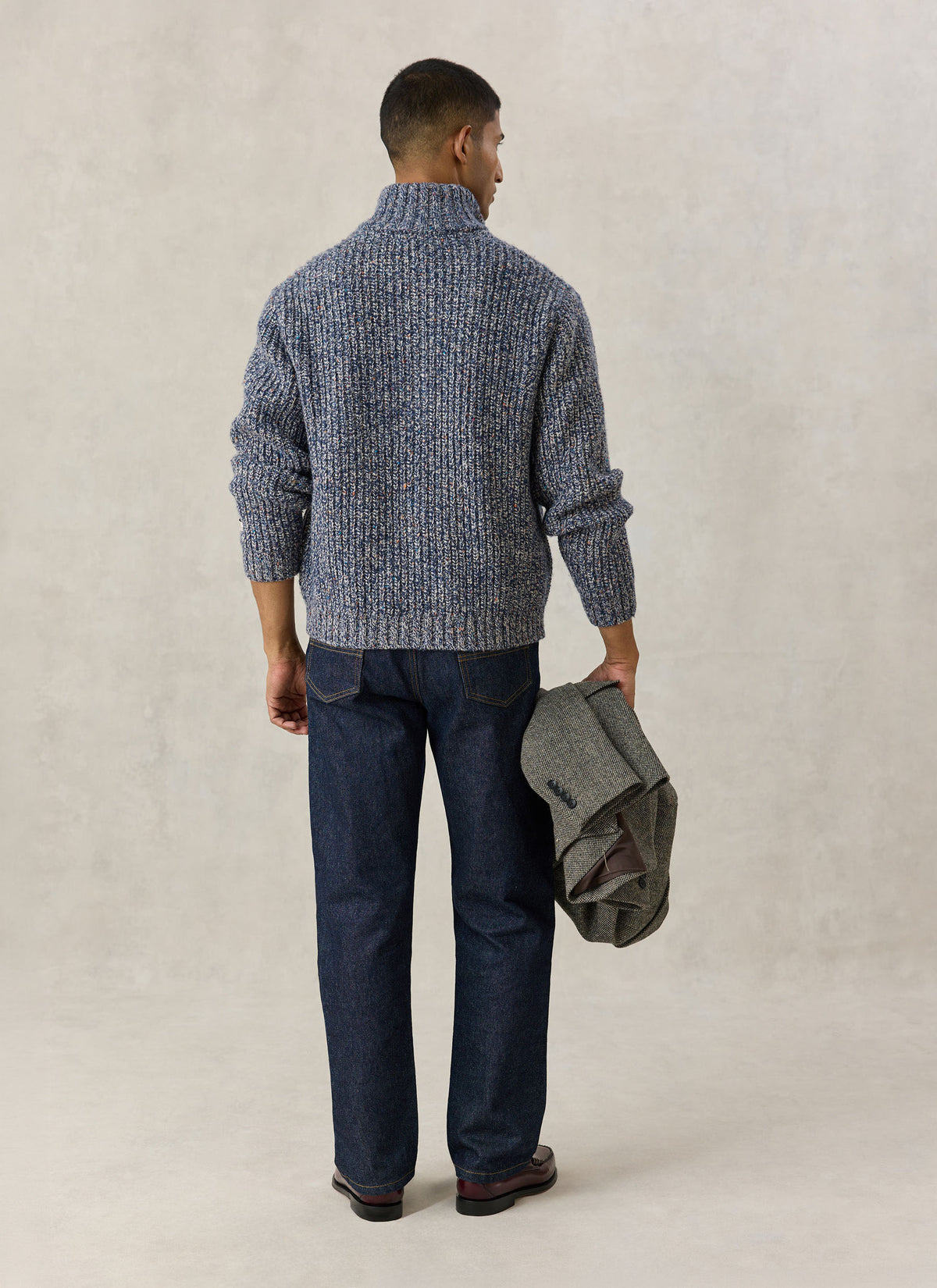 A model from the back wearing the Percival blue fleck Norton zip cardigan with dark jeans and holding a jacket.