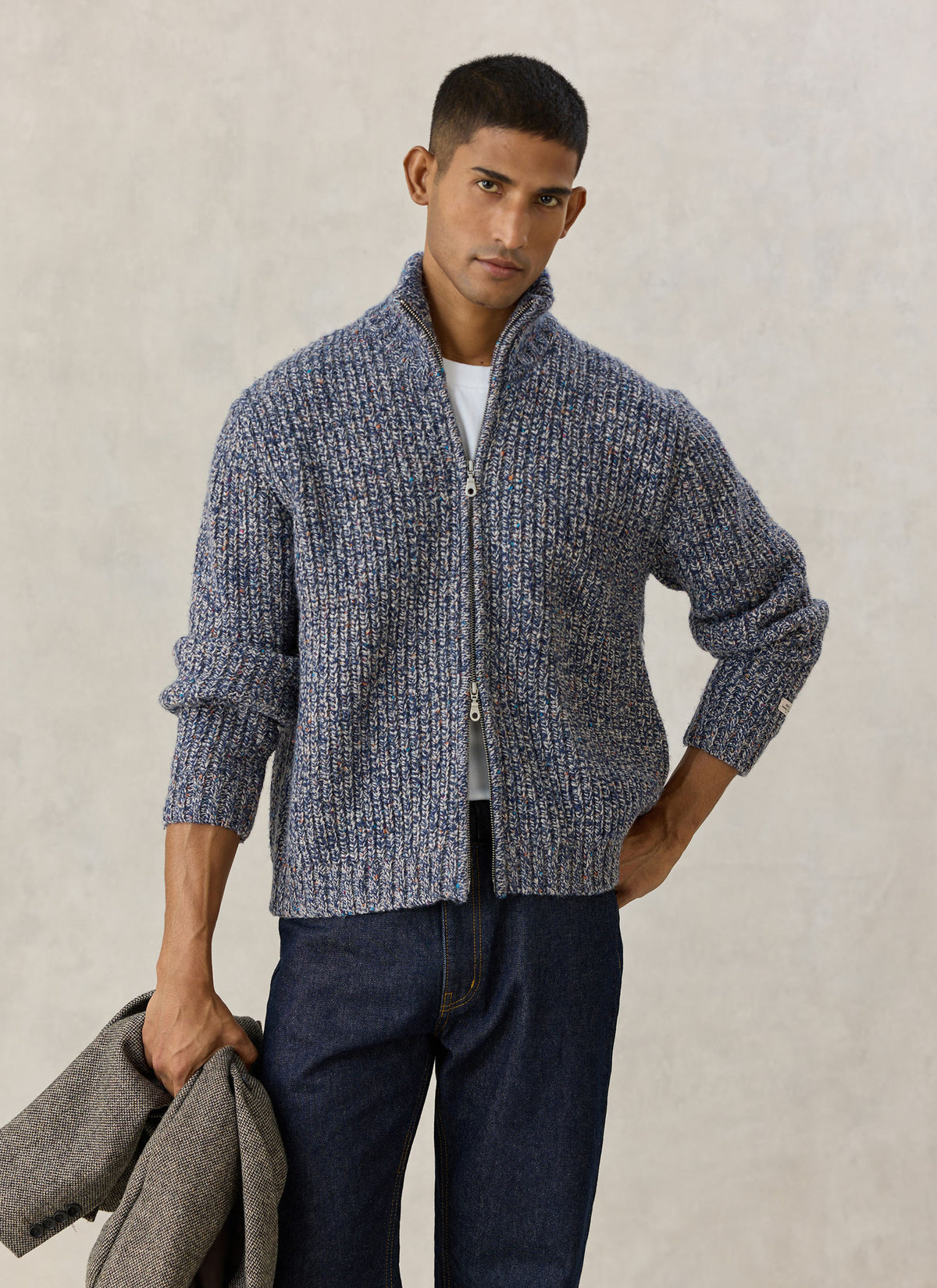 Model wearing the blue fleck Norton ribbed zip cardigan over a white tee and jeans against a studio backdrop.