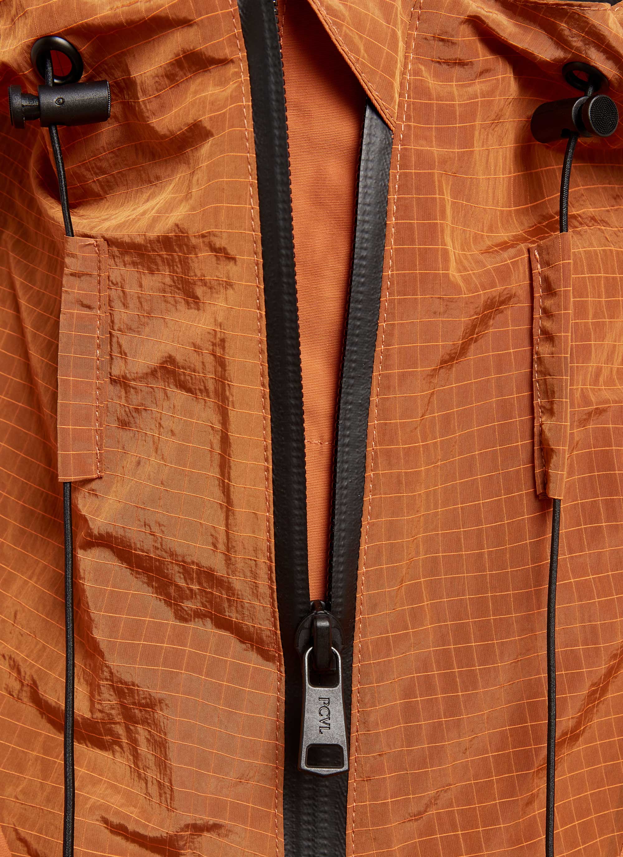 A close-up of the Percival PCVL Zip Through Jacket in rust, detailing the technical zip, hood toggles, and ripstop fabric.