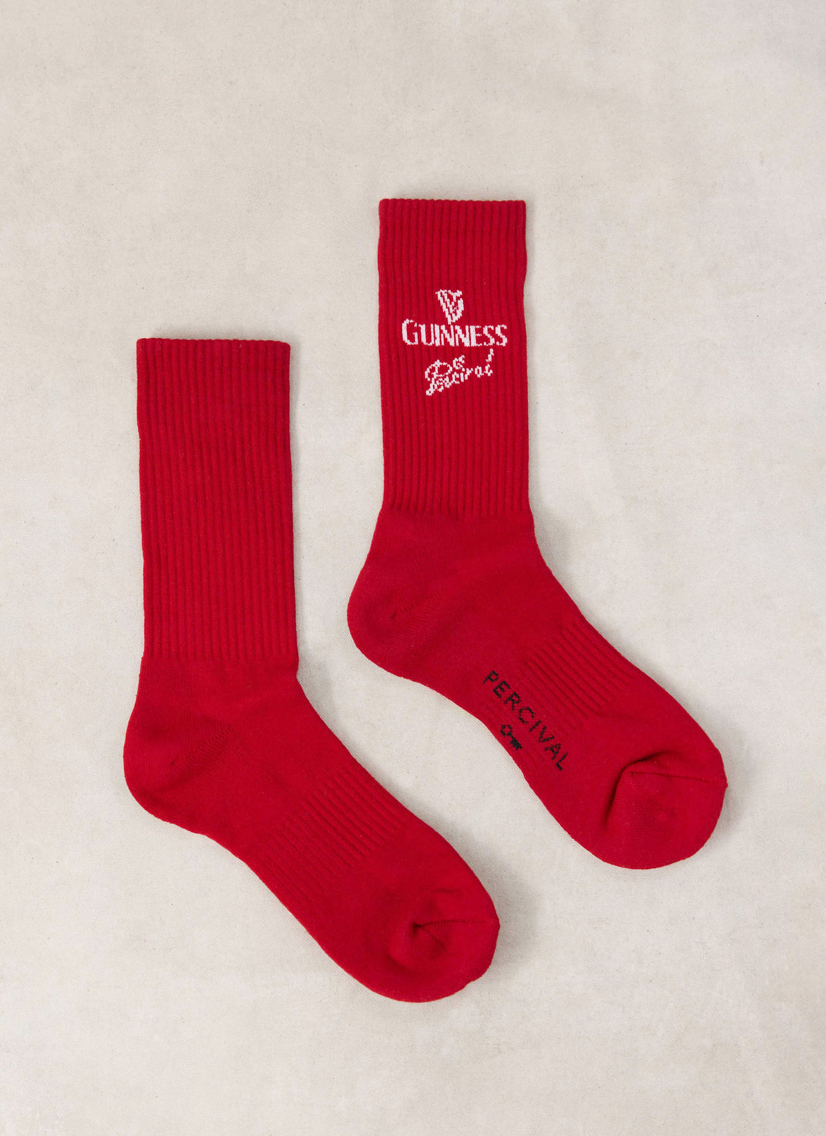 Flat lay of red Guinness x Percival cotton blend crew socks featuring white logo detailing.