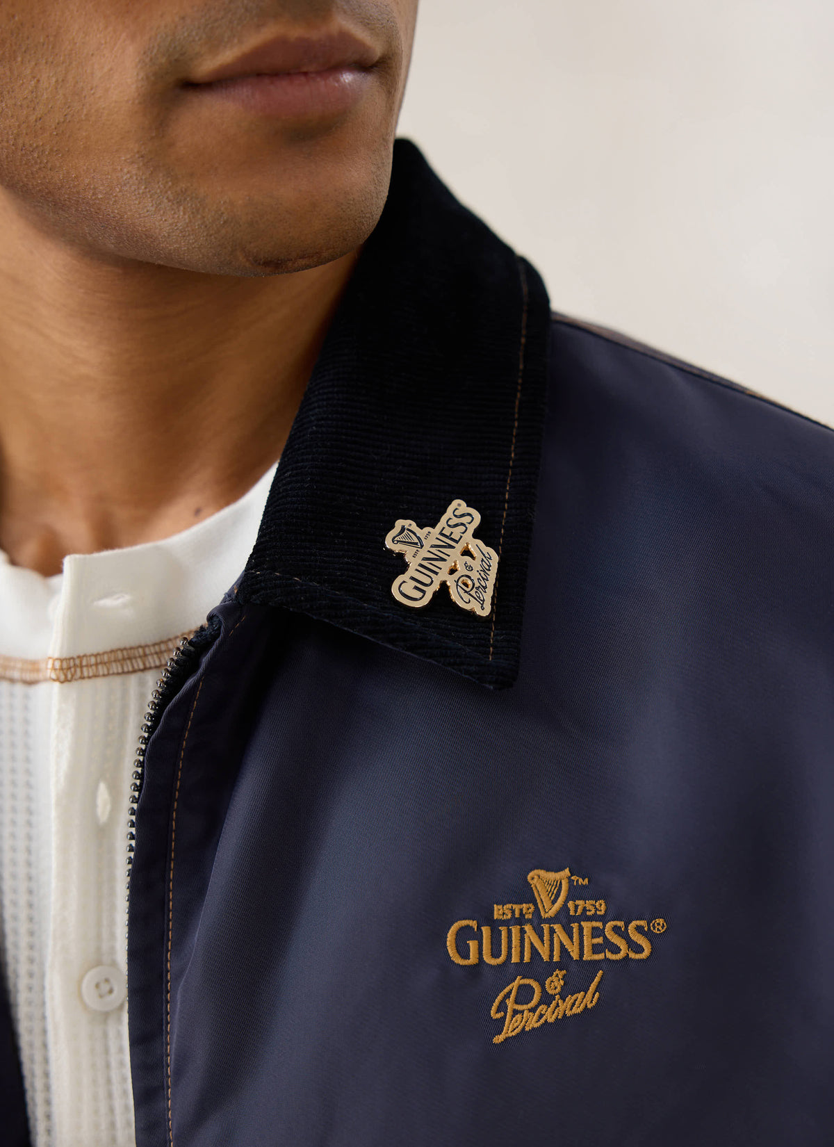 Close-up of a model wearing the Guinness x Percival navy nylon jacket, highlighting the gold embroidery and collar pin.