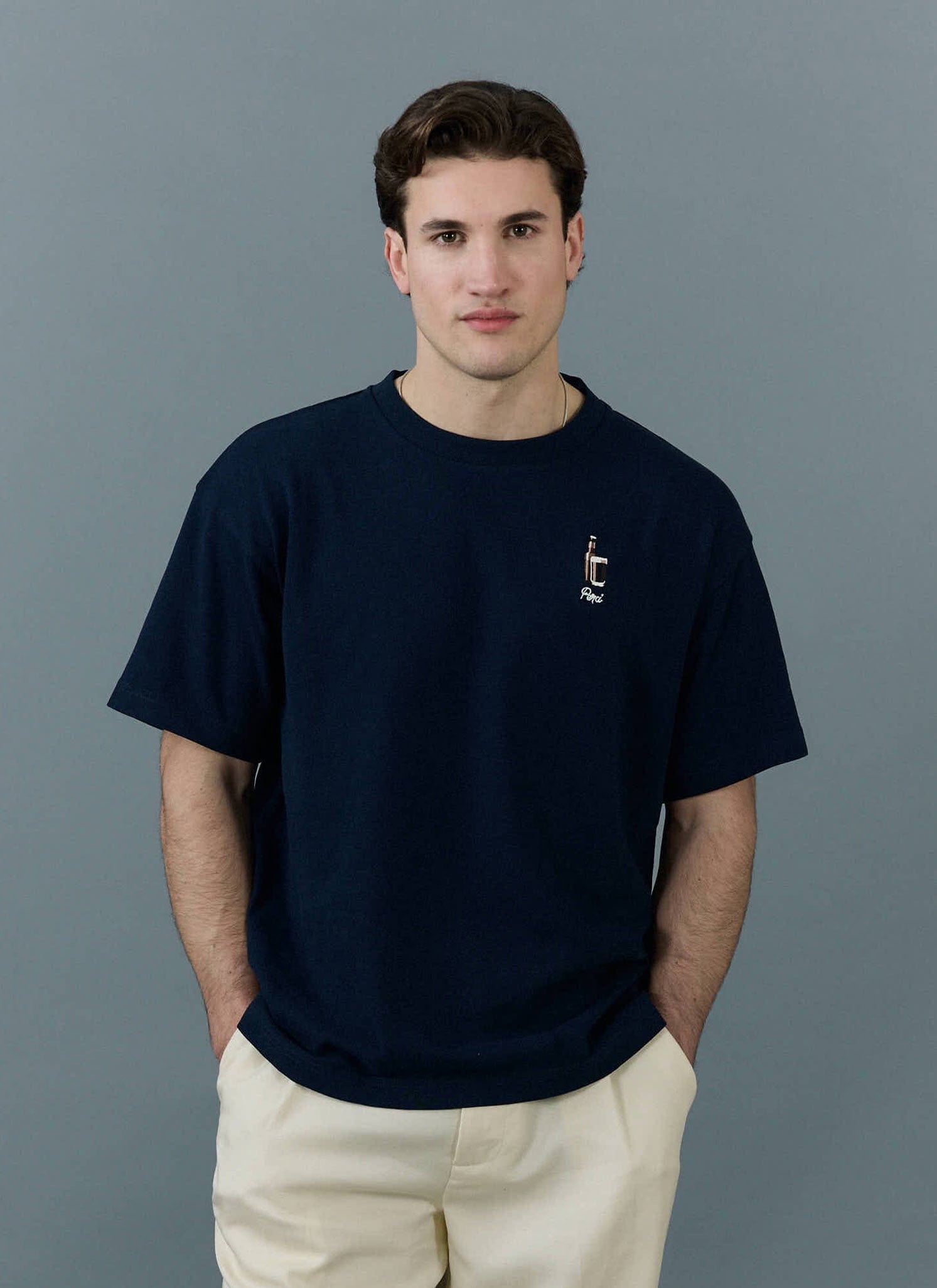 A model wears the navy Percival Stout Oversized T Shirt, featuring stout embroidery, styled with cream trousers.