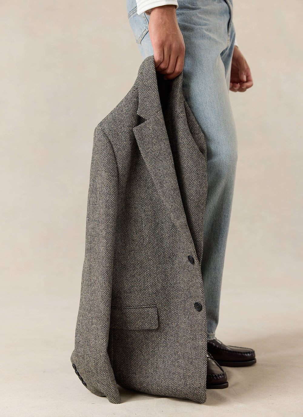 Percival Wilde Tailored Blazer in grey birdseye wool held by a model wearing light wash jeans and dark loafers.