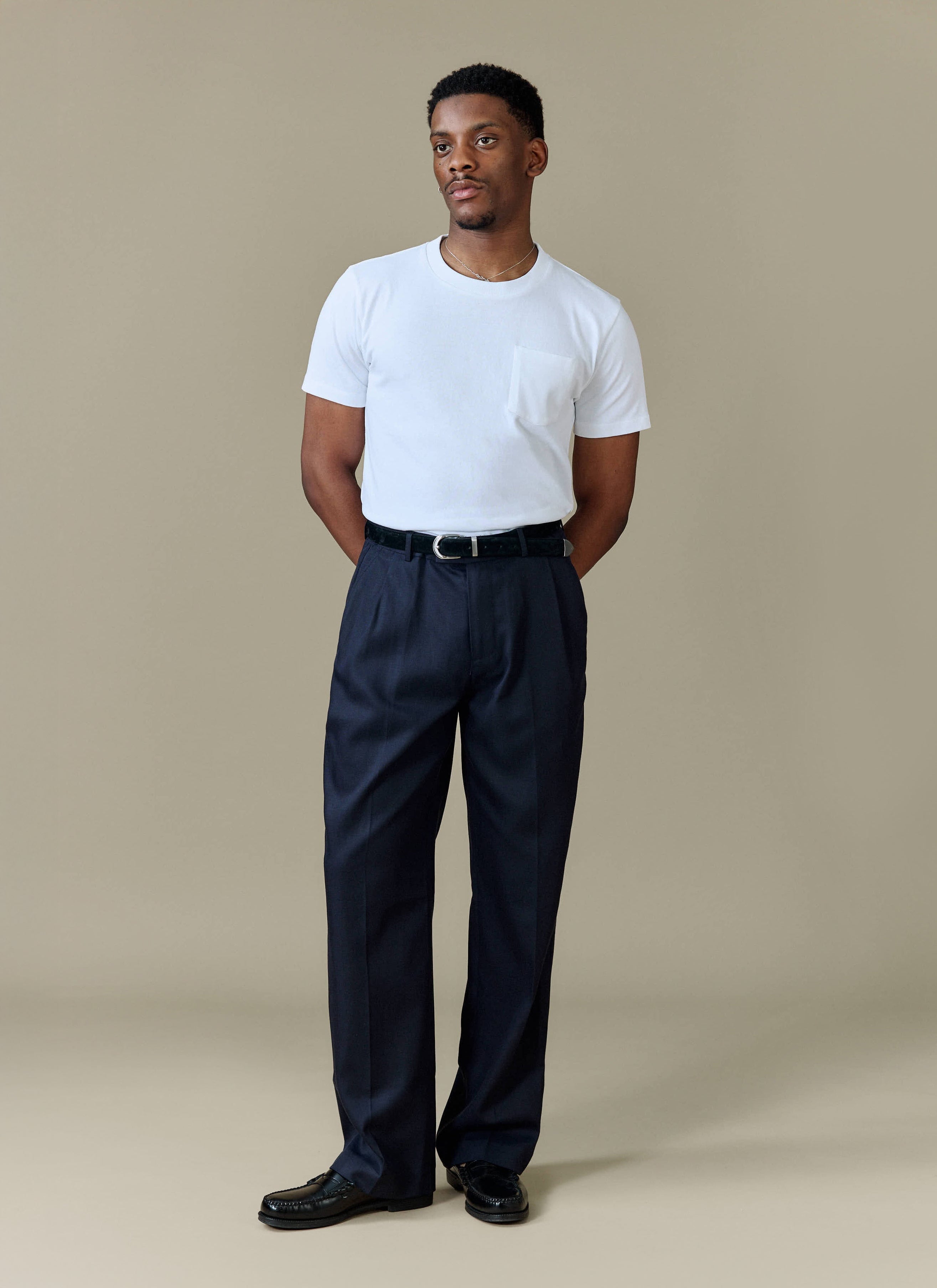 A model styles the Percival navy Pleated Leg Trousers with a classic white pocket t-shirt and black leather loafers.