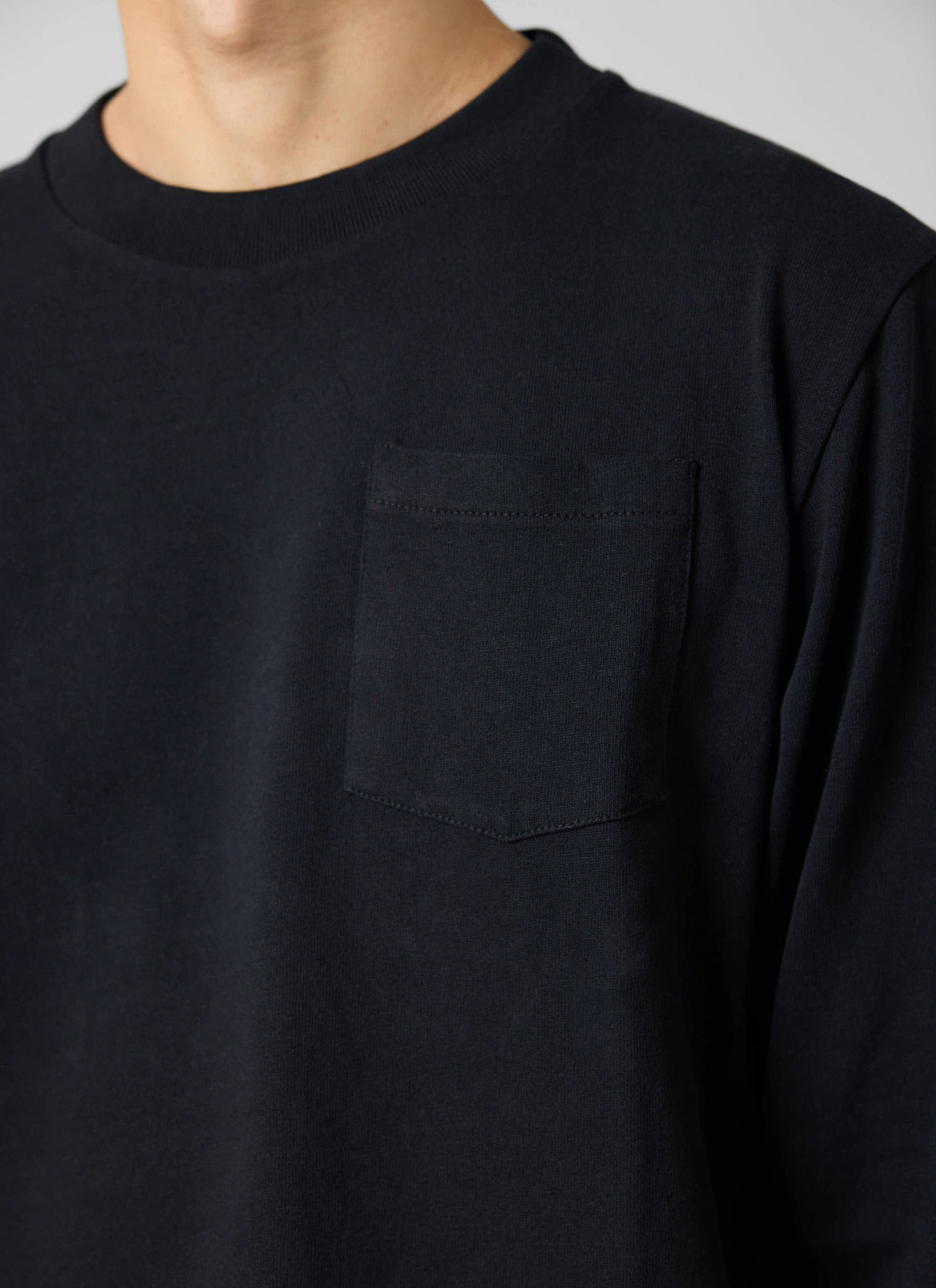 A close-up of a model wearing the Percival Long Sleeve Pocket T Shirt in black, showing the chest pocket and neckline.