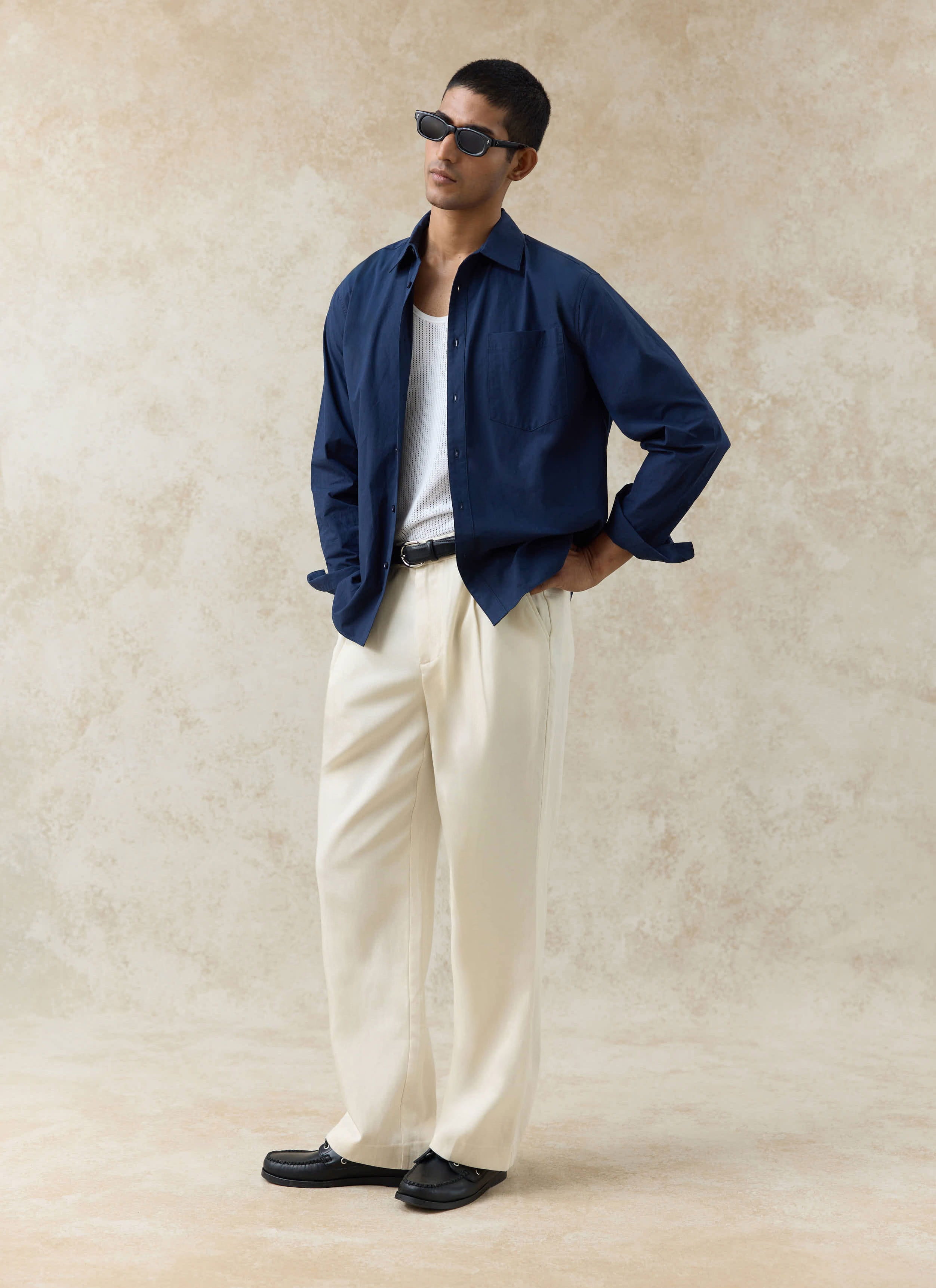 Navy cotton Percival Dali Relaxed Poplin Shirt, styled open over a white vest and cream trousers on a model.