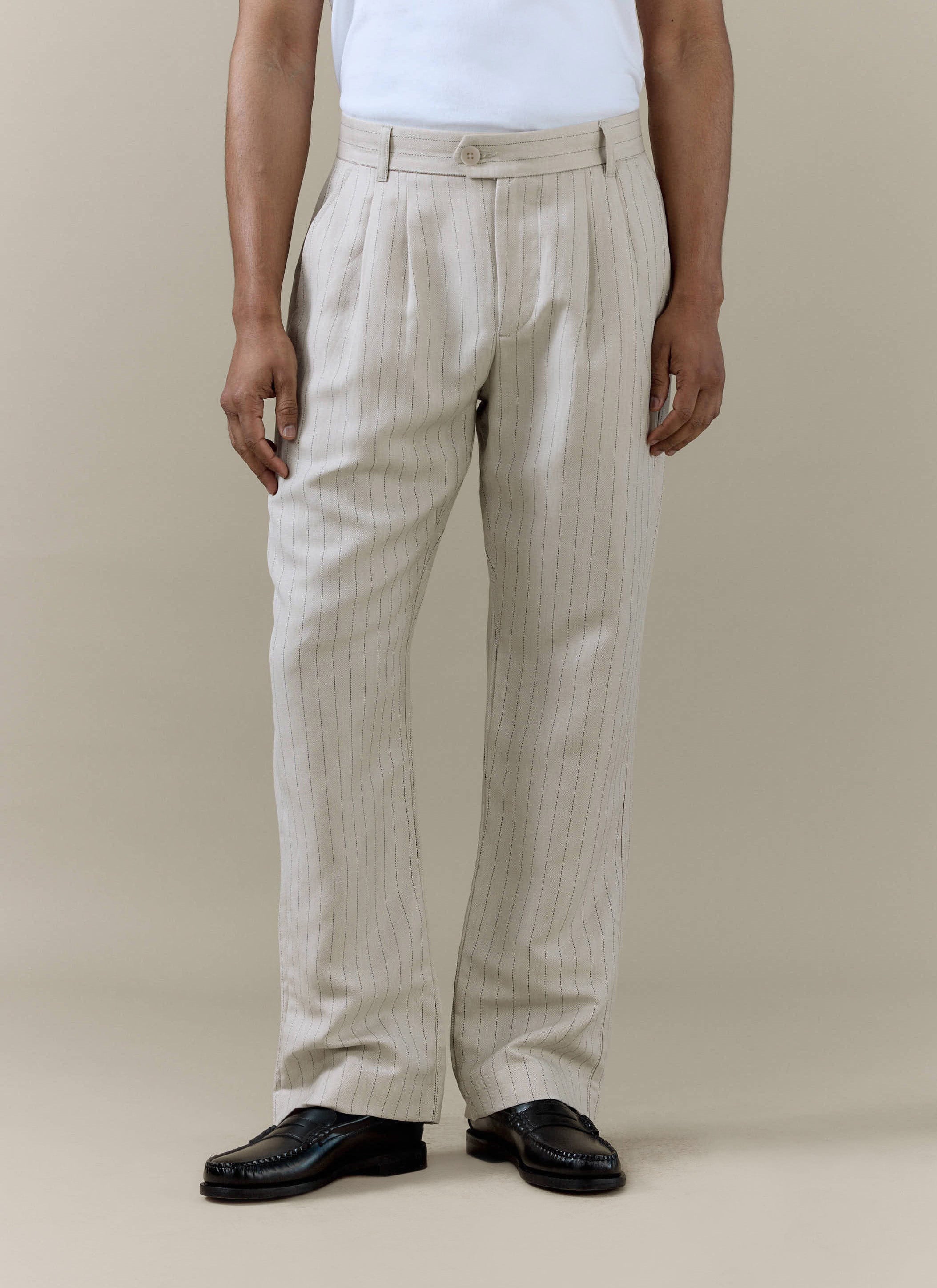 A model wears the cream striped pleated tailored trousers from Percival, styled with a white t-shirt and black loafers.