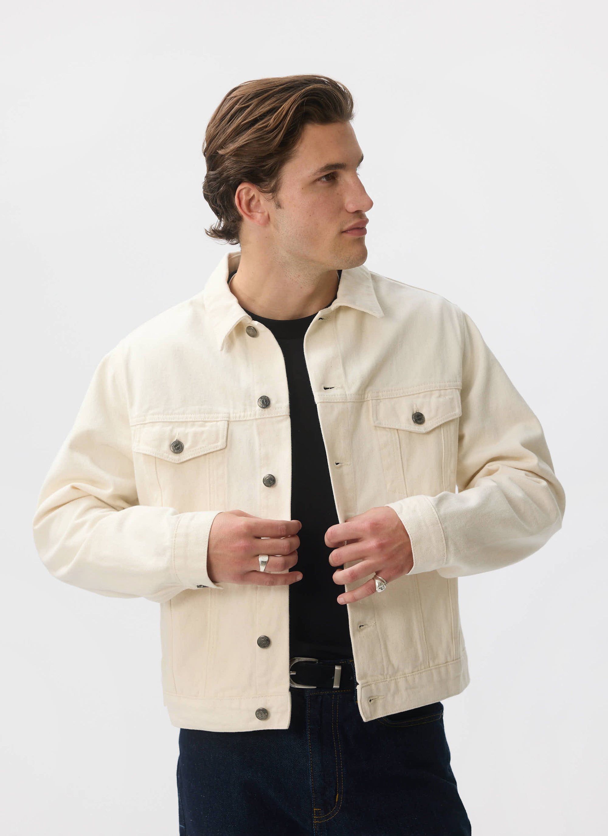 A model wears the ecru denim Western Trucker Jacket from Percival, styling it over a black t-shirt and jeans.
