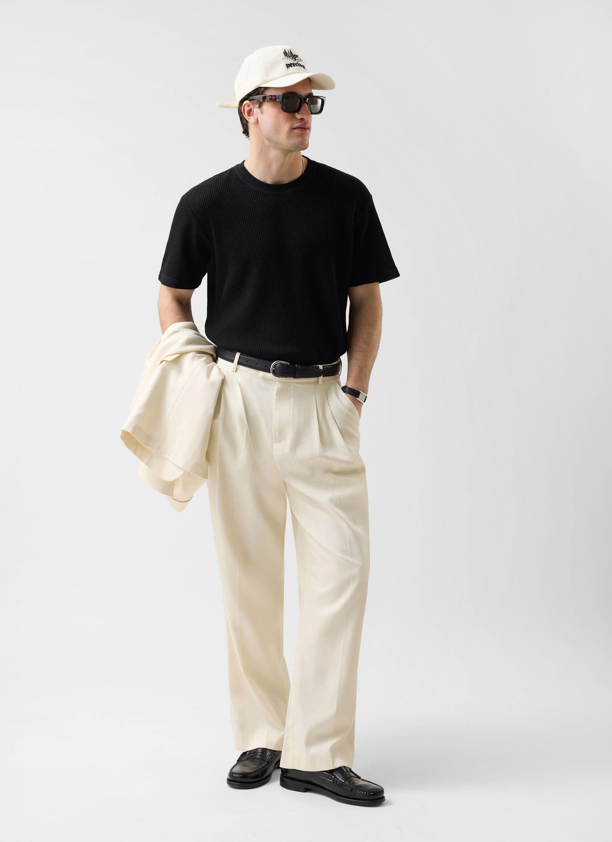 Full-length shot of a model styling the Percival black Waffle Short Sleeve T-Shirt with cream trousers and accessories.