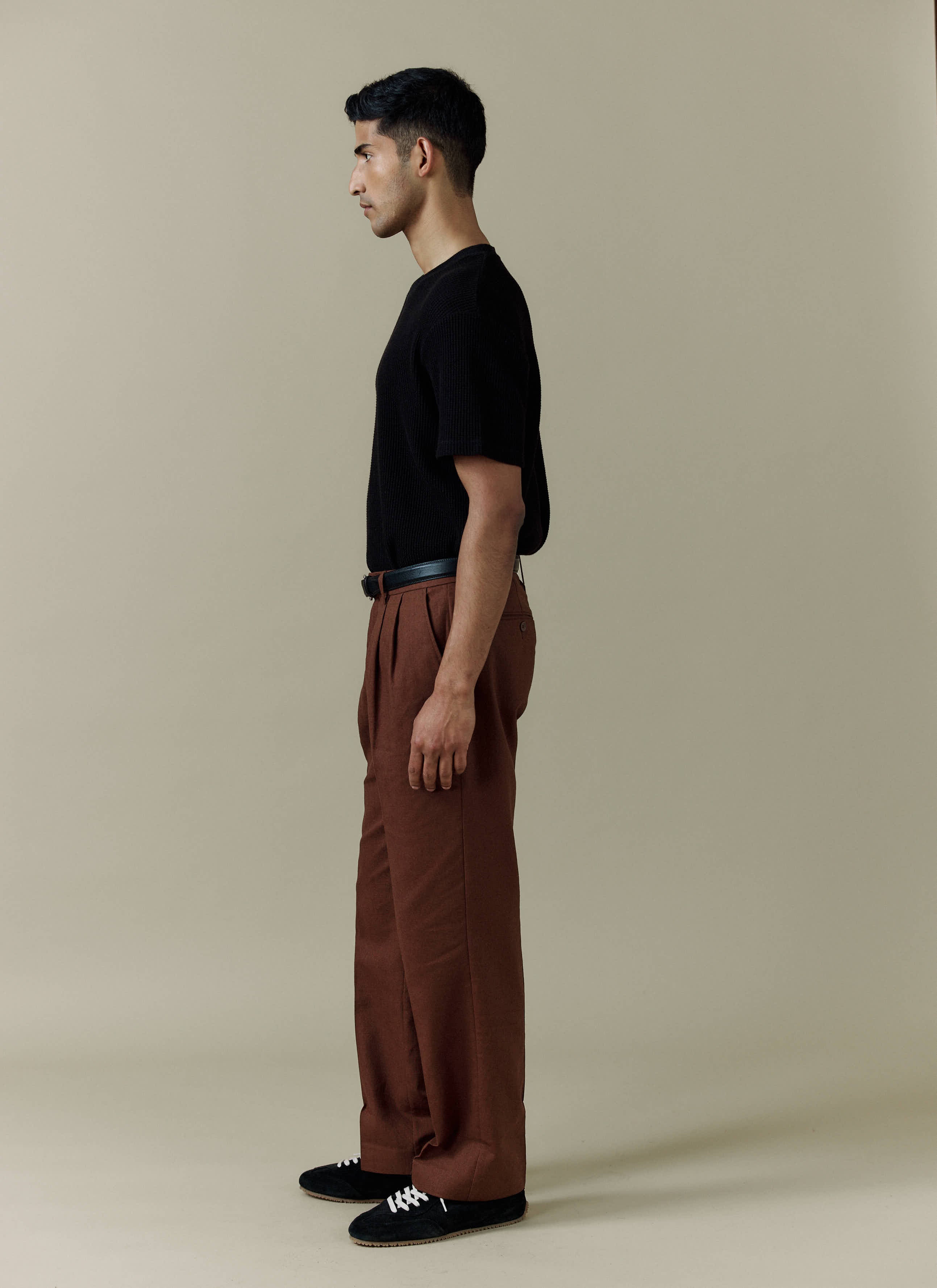 Side view of a model wearing the Percival Pleated Tailored Trousers in brown linen with a black t-shirt.