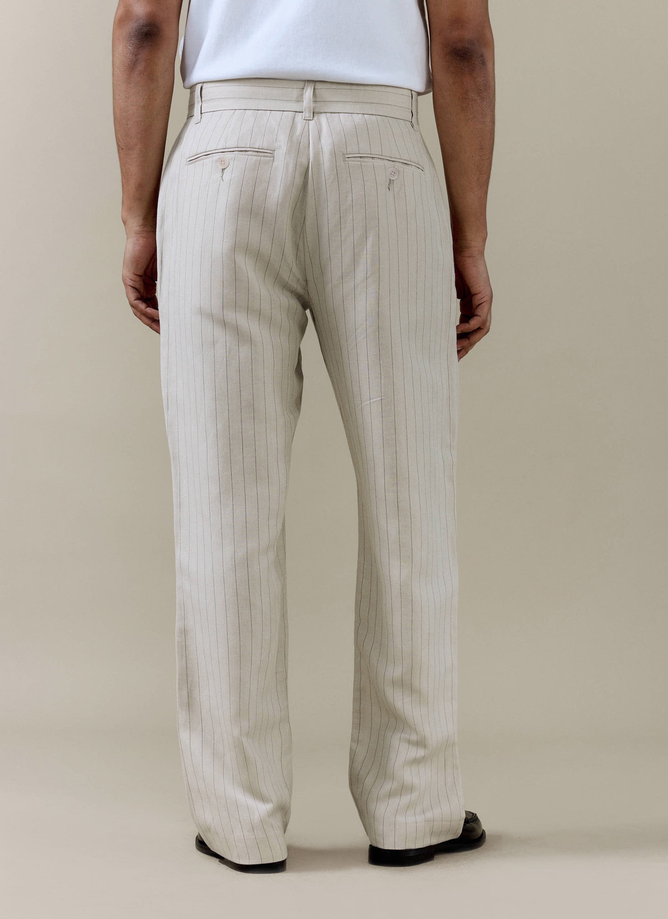 A model wears the cream striped pleated tailored trousers from Percival from the back, paired with a white t-shirt.