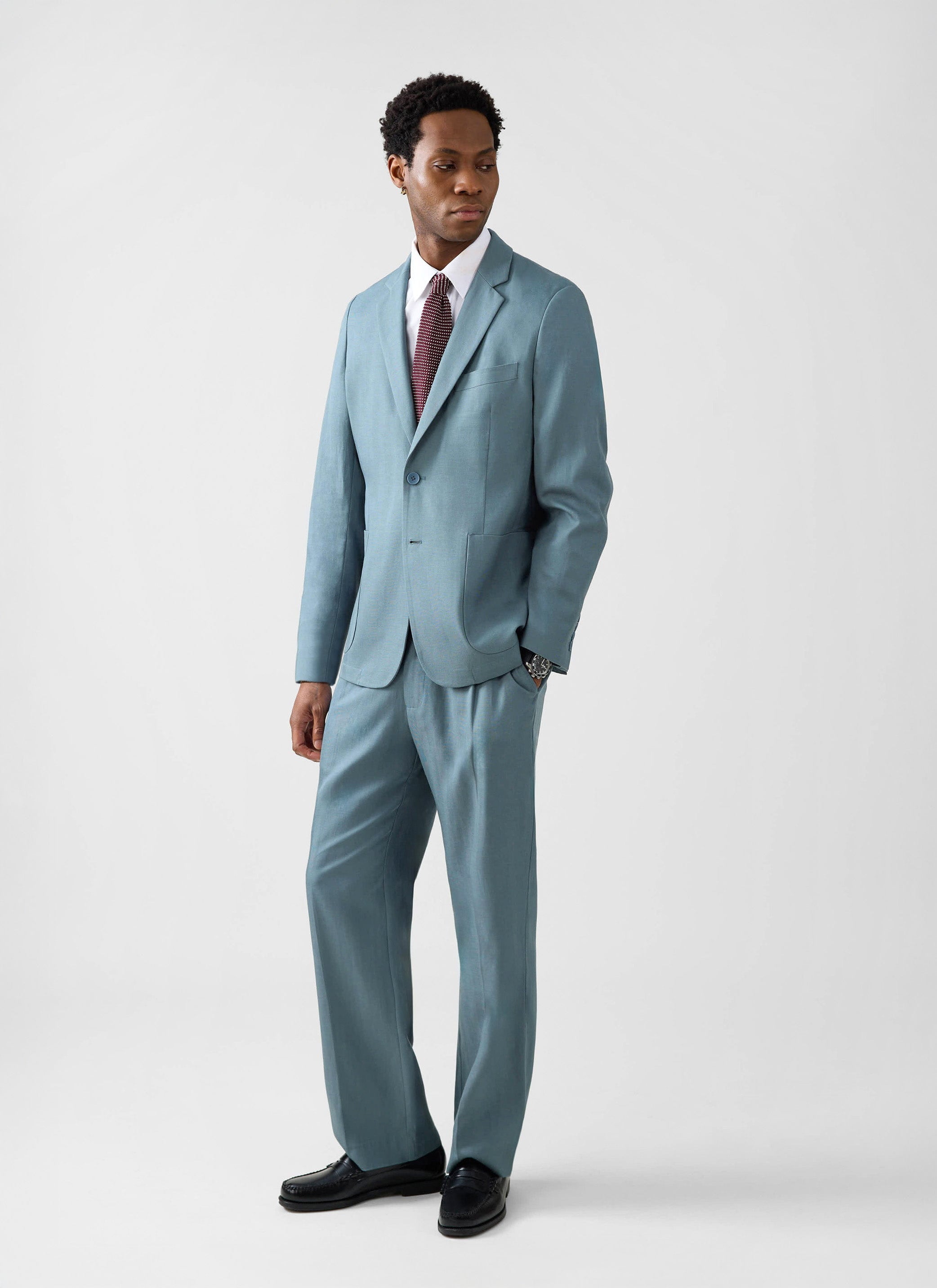 A man models the Percival Lyocell Regular Blazer in Slate Blue with matching trousers against a studio background.
