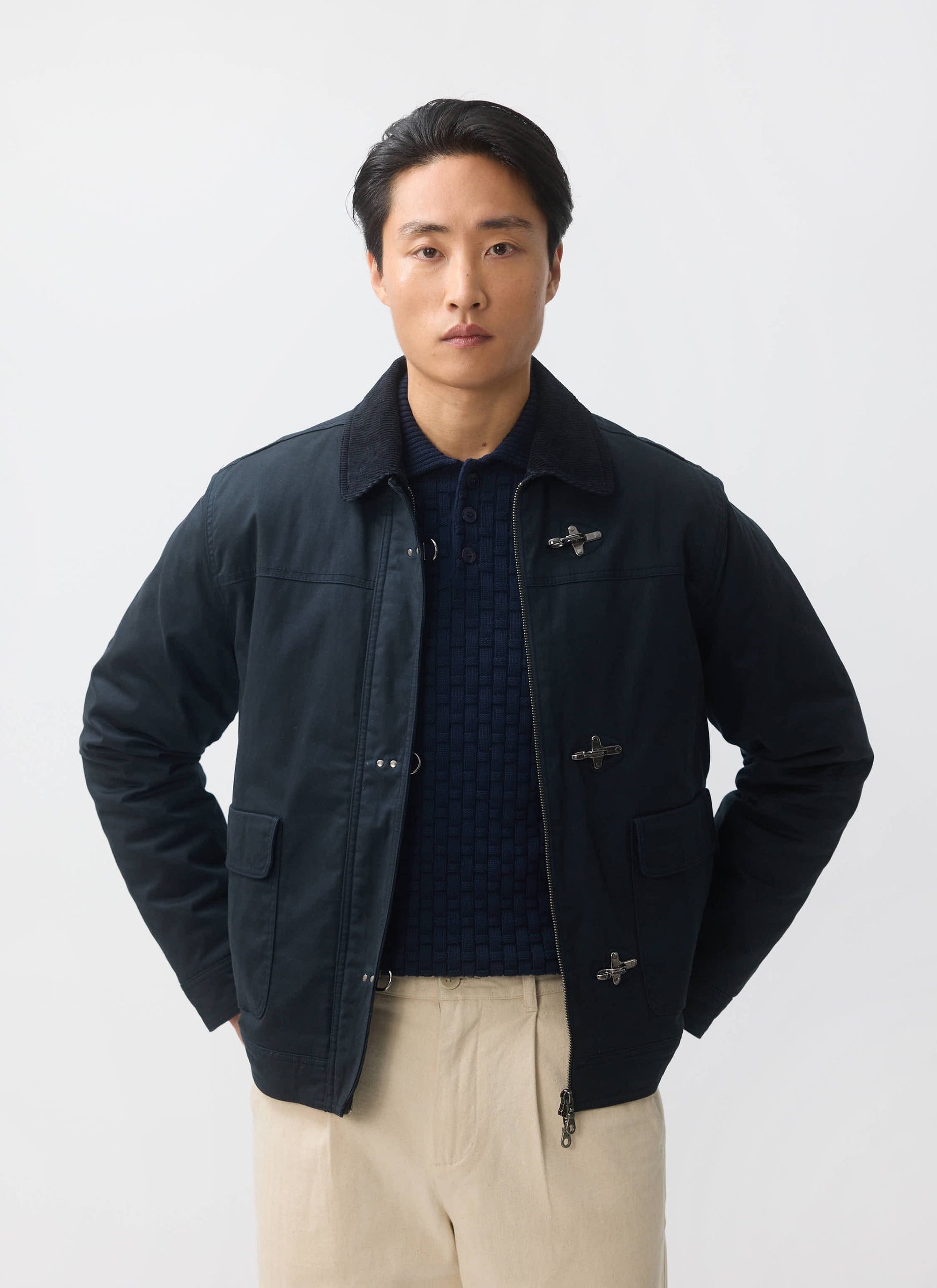 A model wears the Percival Fontane Wax Jacket in navy, styled over a knitted polo and beige trousers.