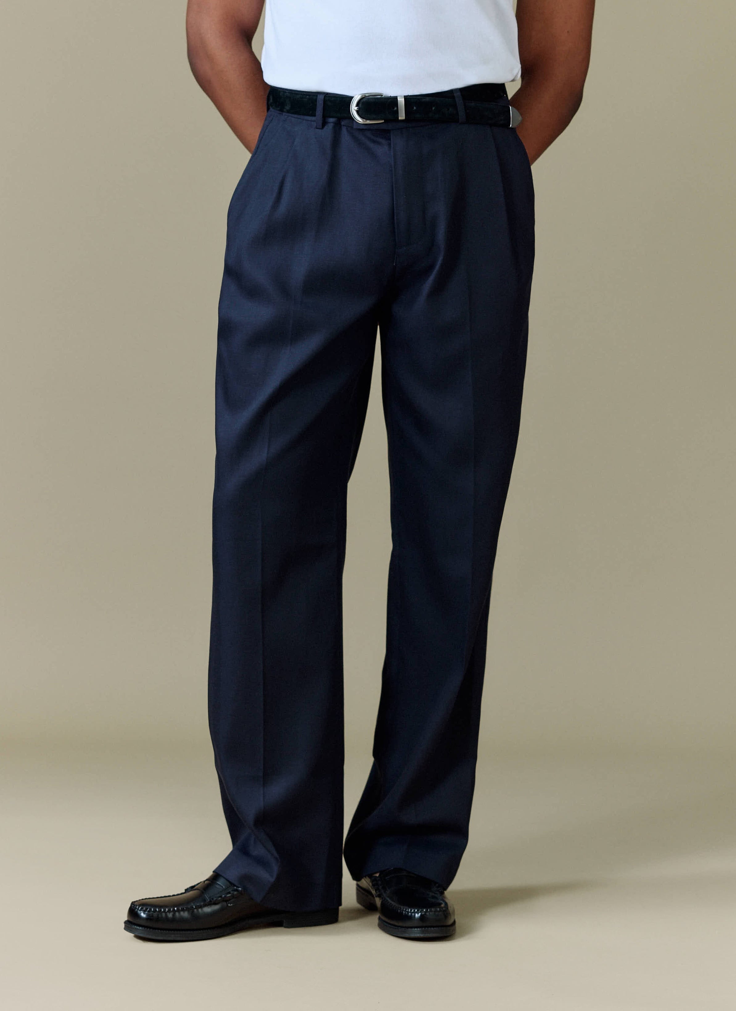 A model wears the navy Pleated Leg Trousers from Percival, styled with a white t-shirt, black belt and black loafers.
