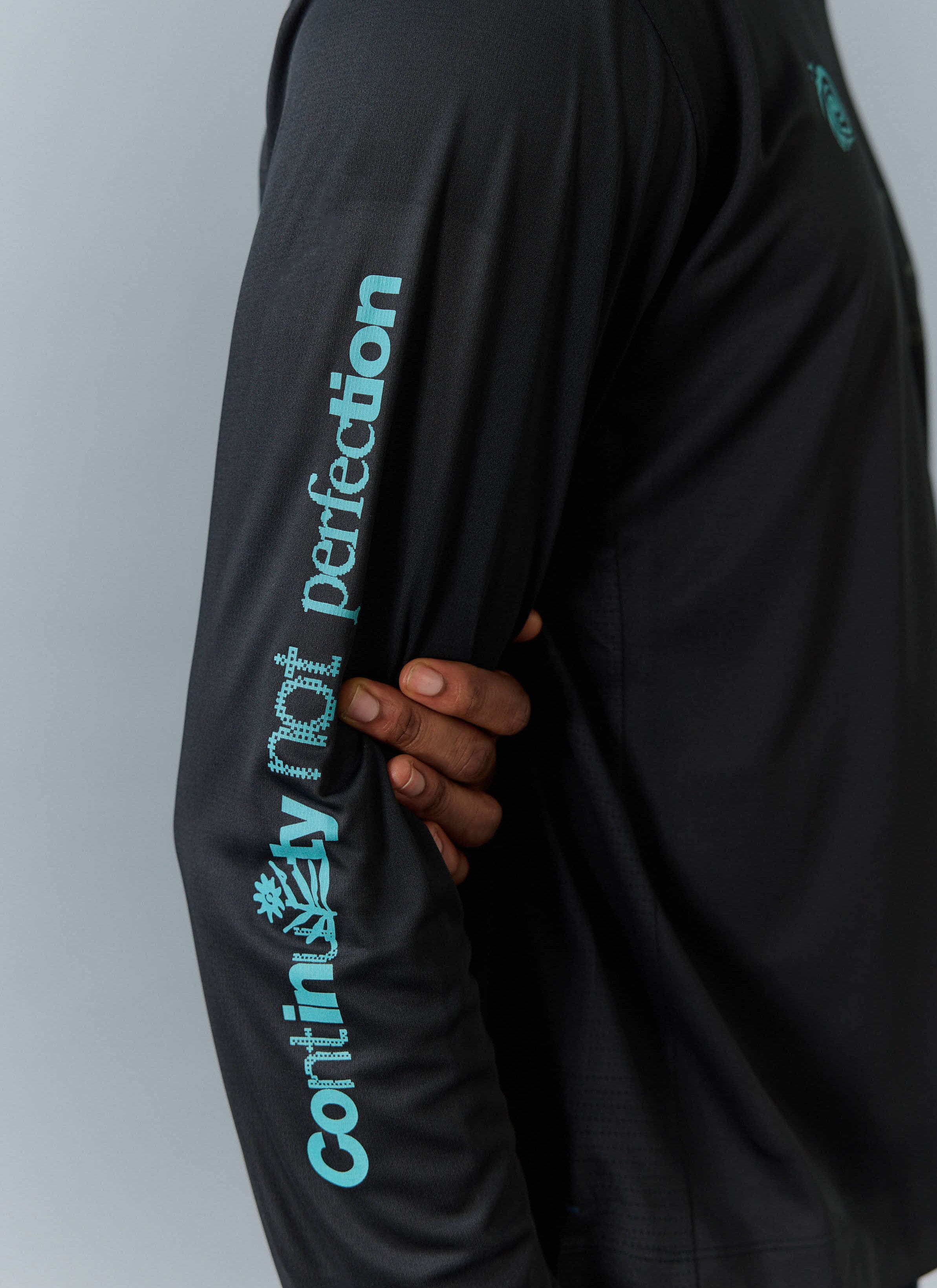 Close-up of the black PCVL Performance Top from Percival, showing the blue 'Continuity not perfection' graphic on the sleeve.