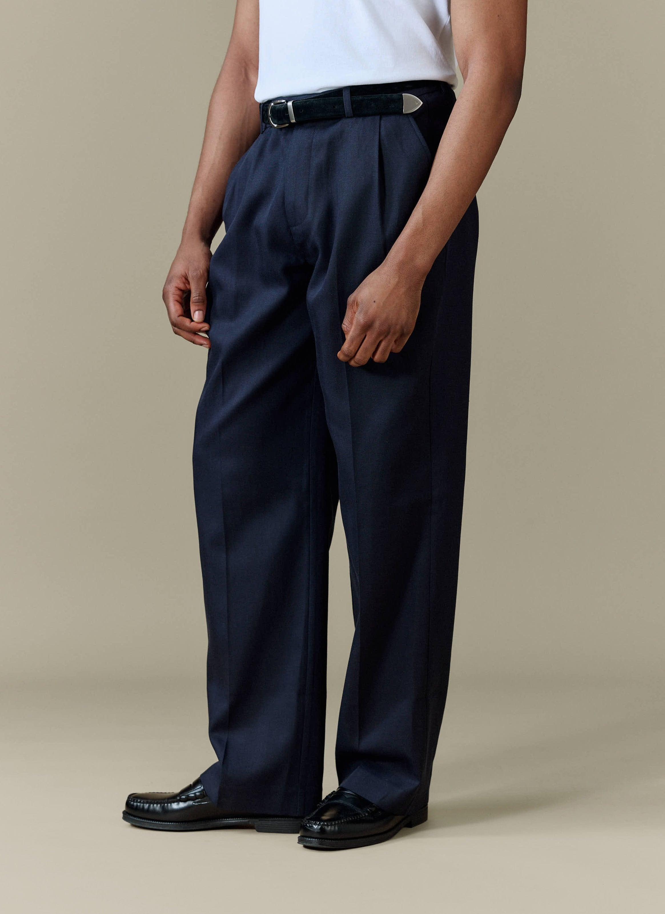 A close-up shot of a model wearing the Percival Pleated Leg Trousers in navy to showcase their relaxed fit and drape.