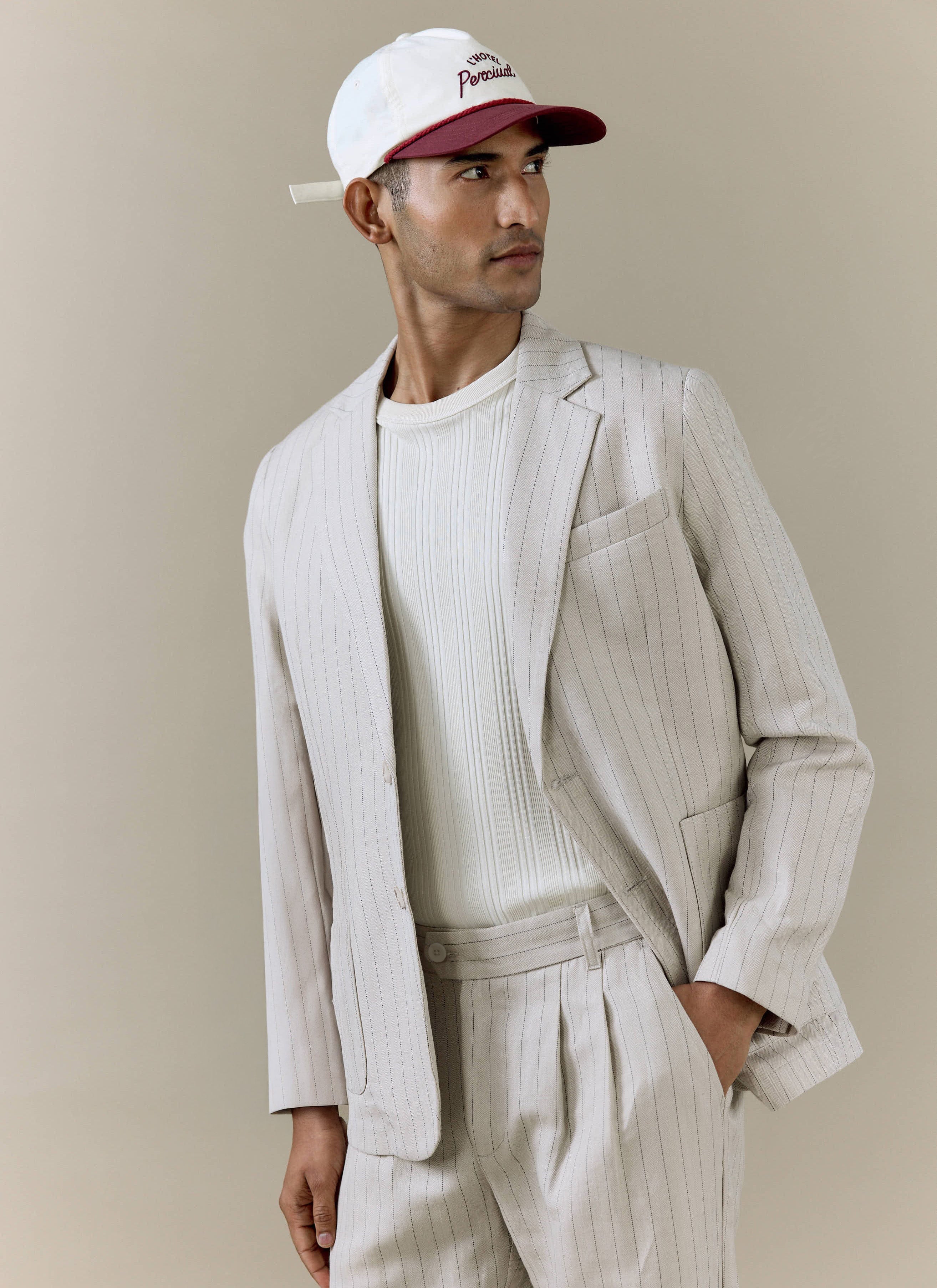 A model wears the cream striped tailored blazer from Percival, paired with matching trousers and a cap.