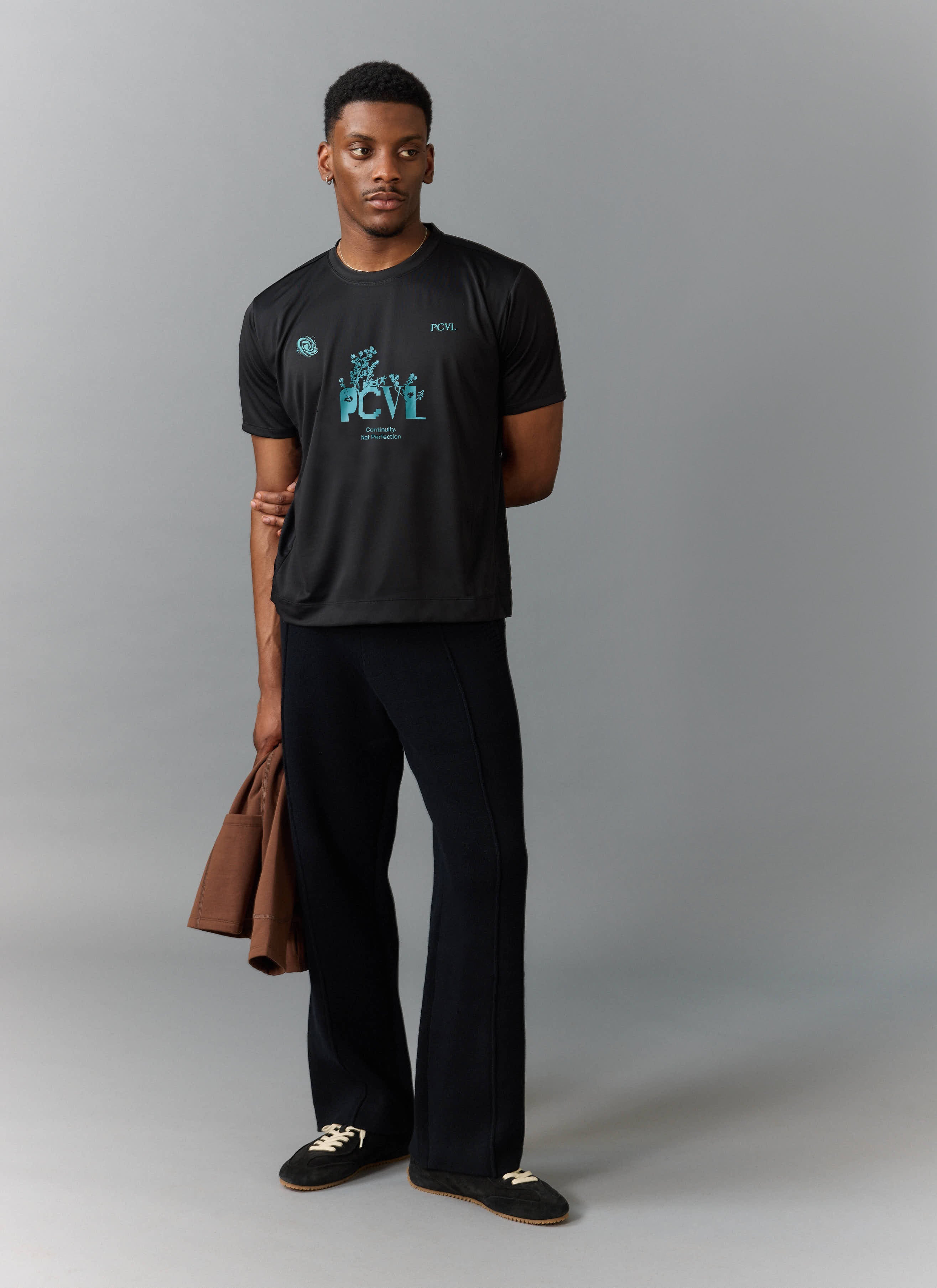 A full-length shot of a model wearing the PCVL Graphic Printed Performance Top in black from Percival.