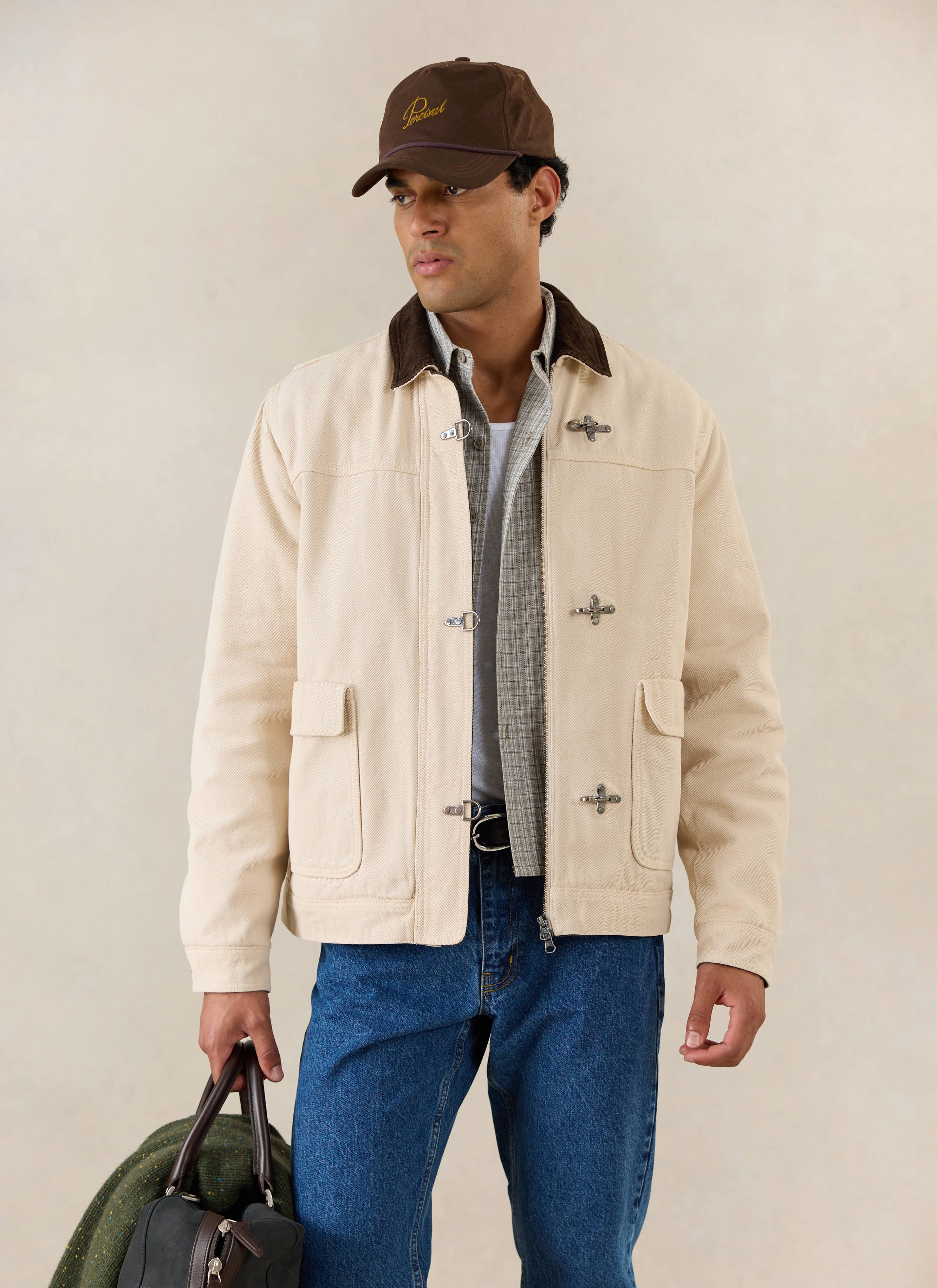 A model wears the Percival cream cotton Fontane Boxy Jacket with metal clasps and corduroy collar, styled with blue jeans.