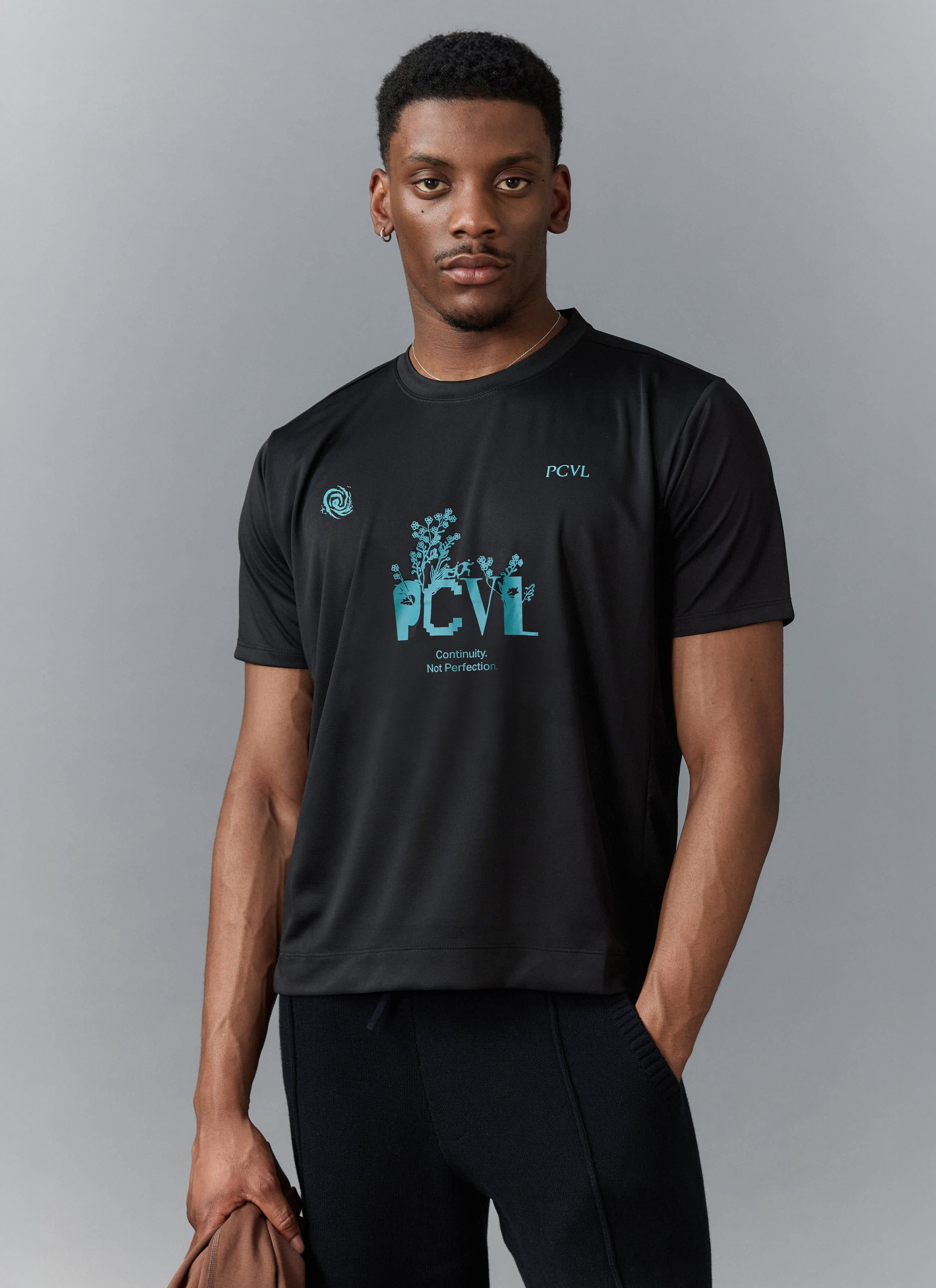 A model wears the Percival PCVL Graphic Printed Performance Top in black, featuring the turquoise floral chest graphic.