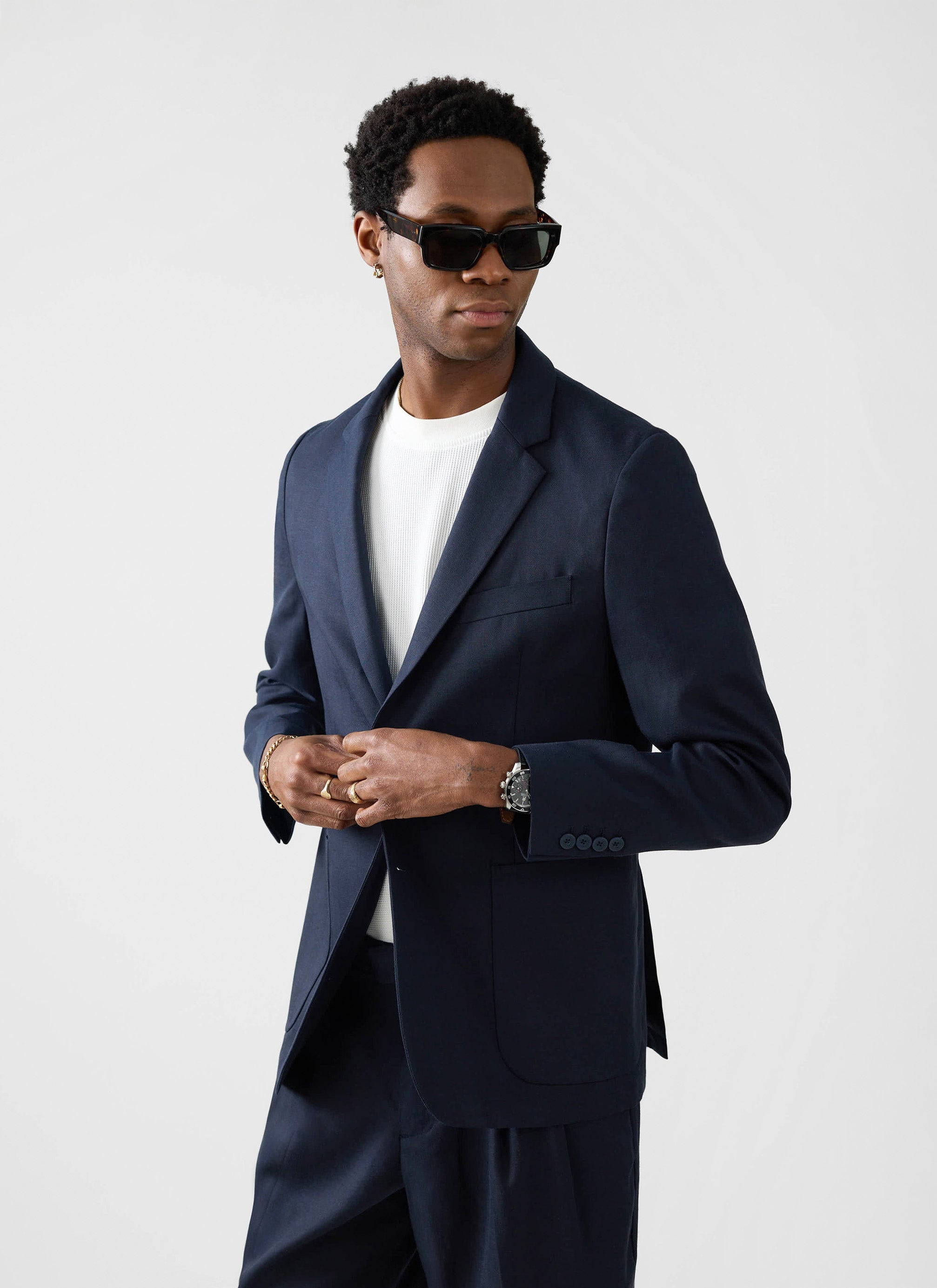 A model wears the Percival Lyocell Regular Blazer in navy, styled with a white t-shirt and black sunglasses.