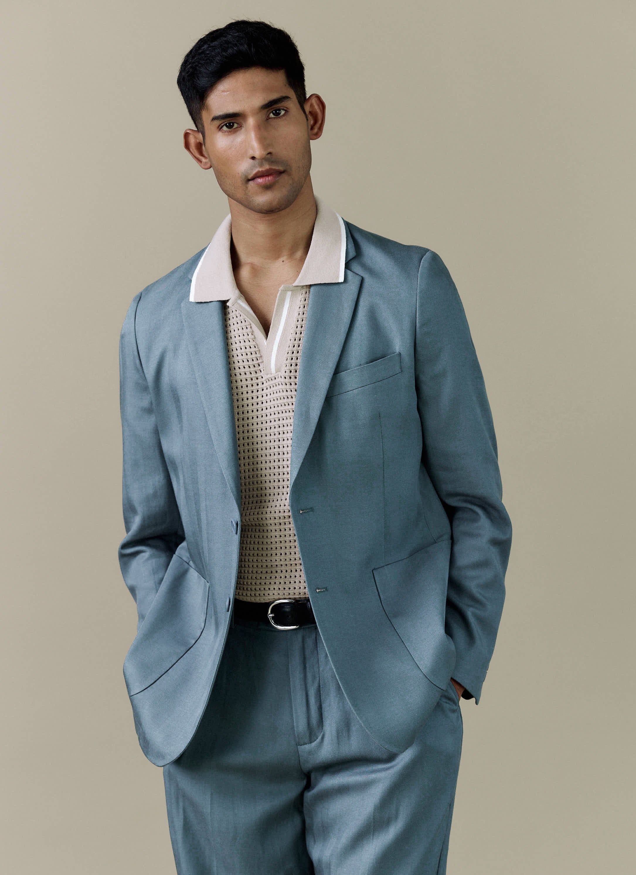 A man models the Percival Lyocell Regular Blazer in Slate Blue, styled over a cream knitted polo shirt.