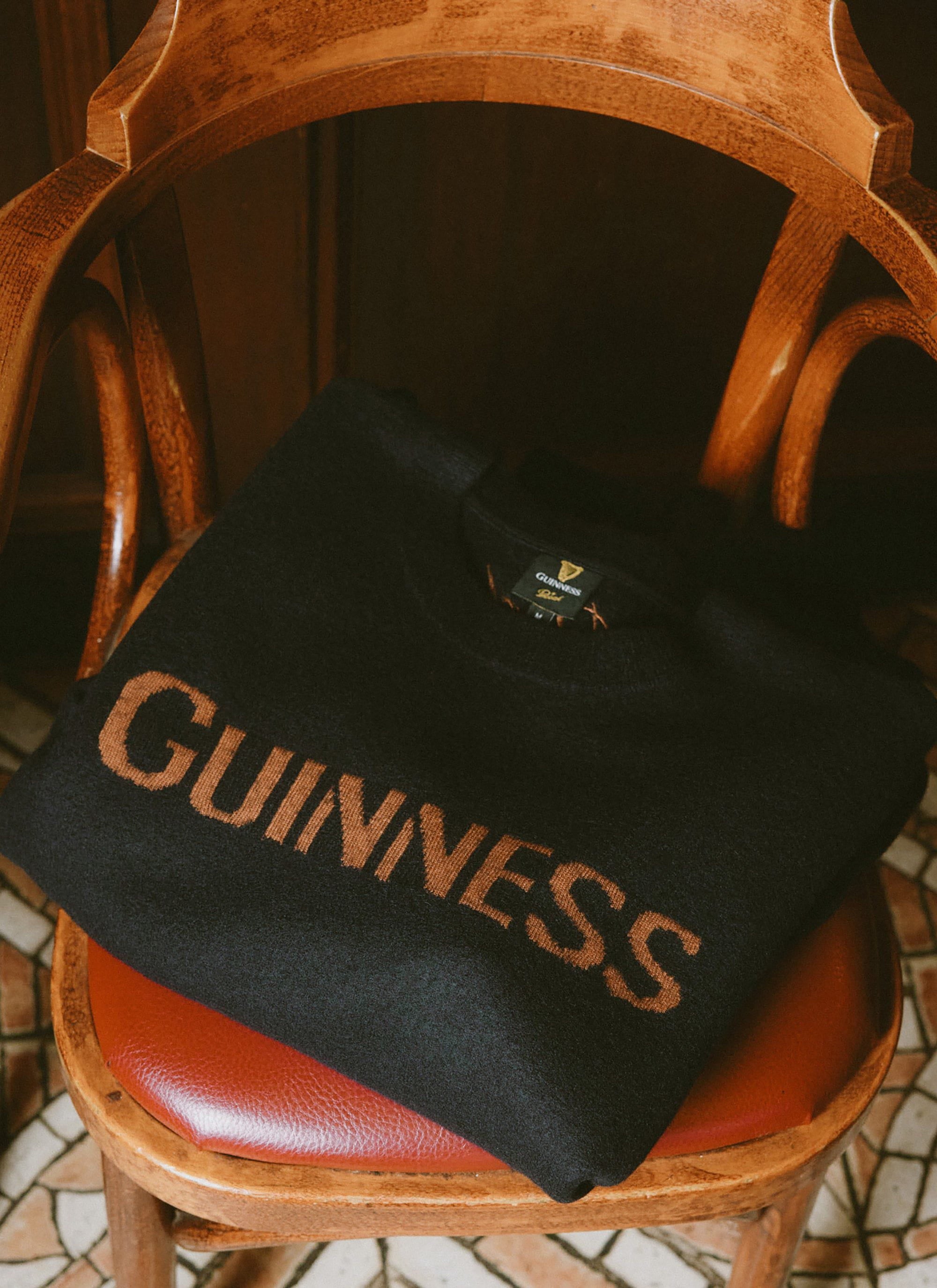 The navy merino wool Guinness jacquard jumper from Percival, placed on the red leather seat of a vintage wooden chair.