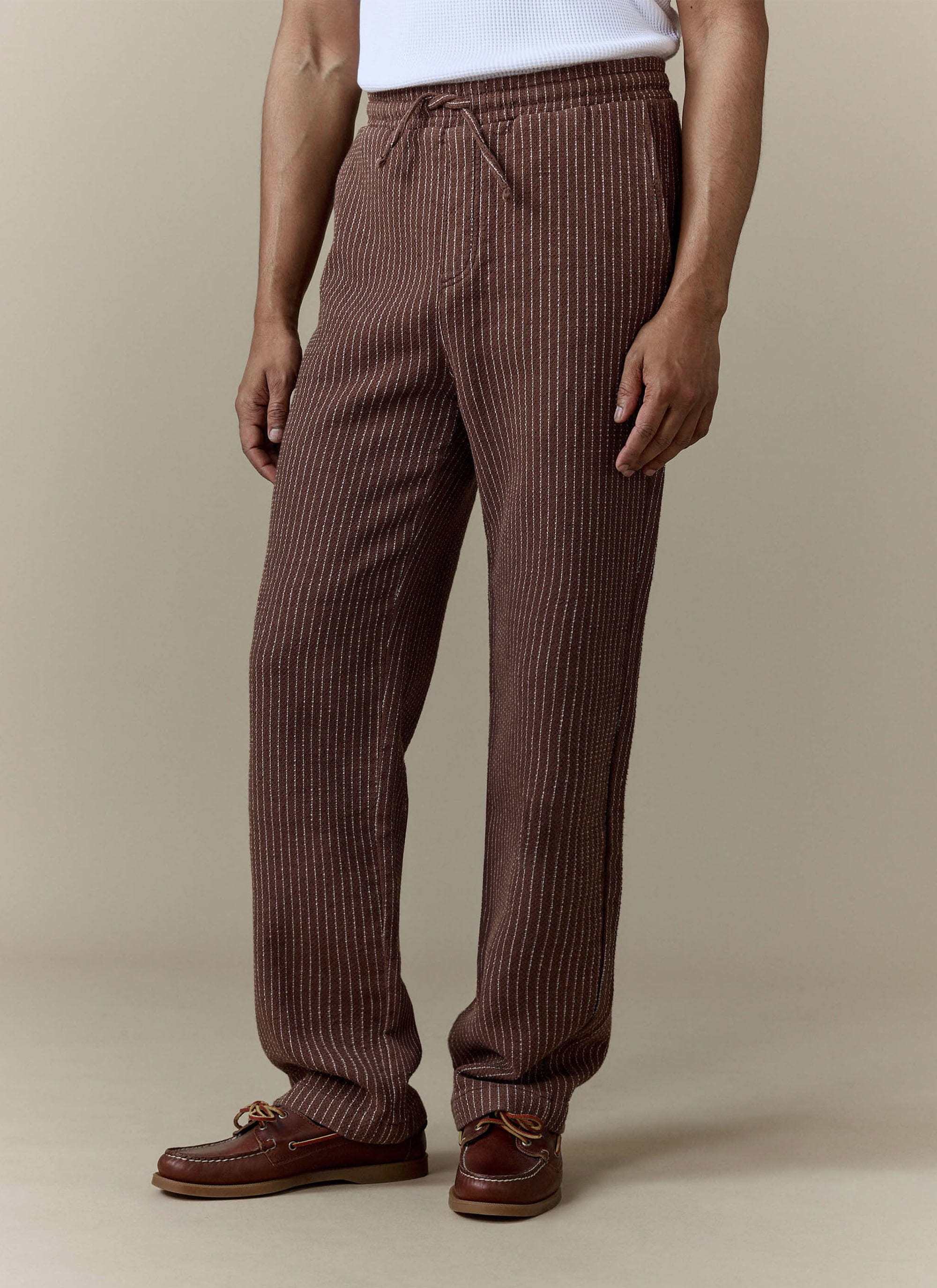 A model wears the brown linen Sorrento Wide Leg Trousers from Percival, styled with a white top and brown boat shoes.