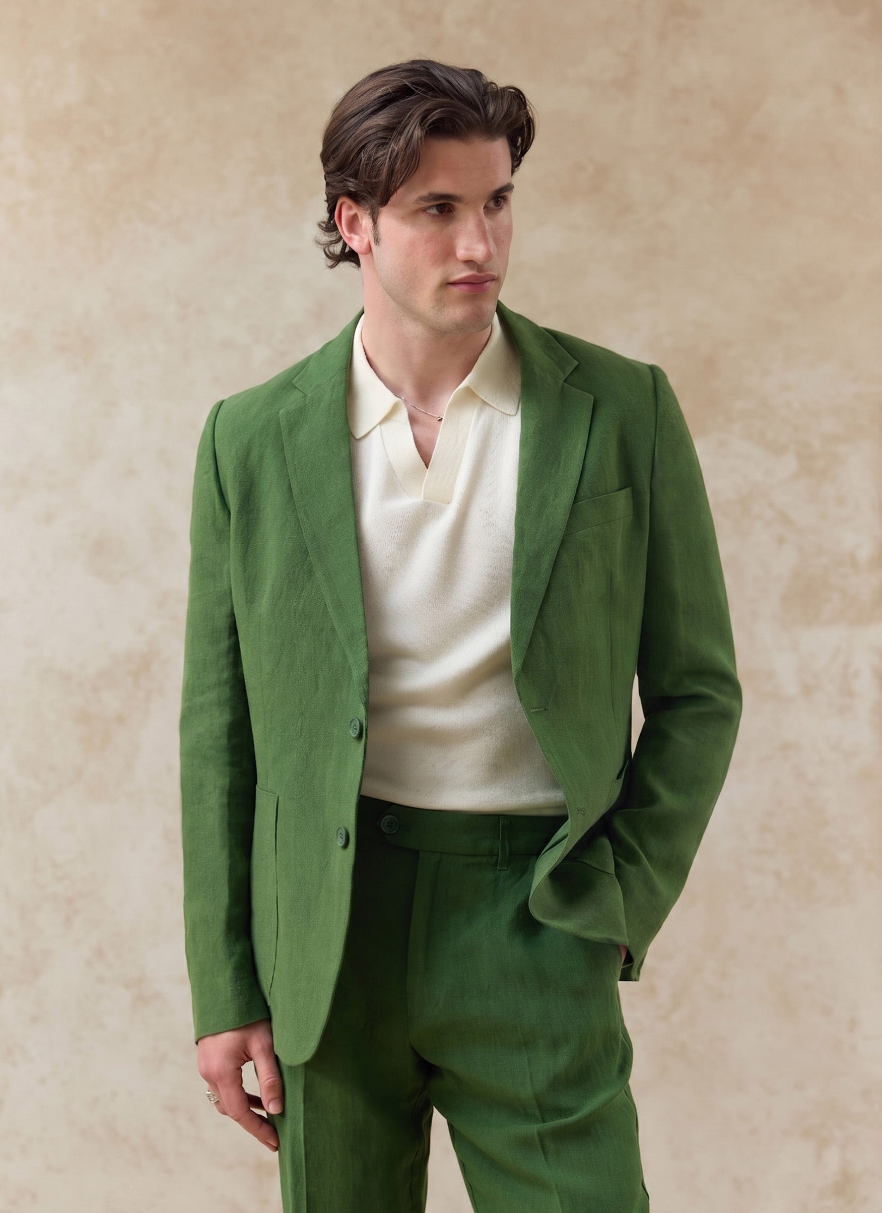 Model wears the forest green Percival Tailored Linen Blazer and matching suit trousers with a cream knit polo shirt.