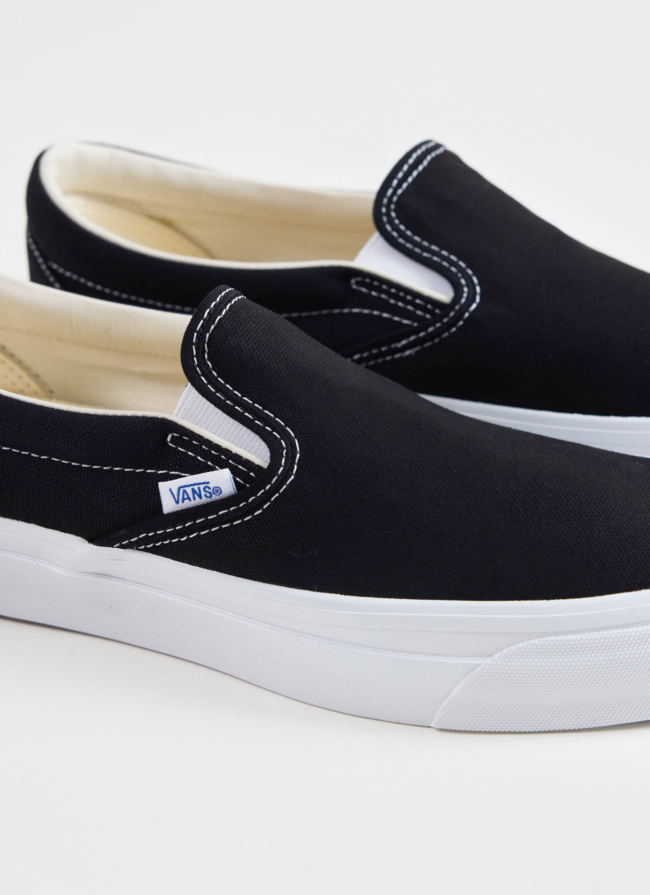 Close-up of the black Vans Slip-On Reissue 98 shoes from Percival, showing the white contrast stitching and logo tag.