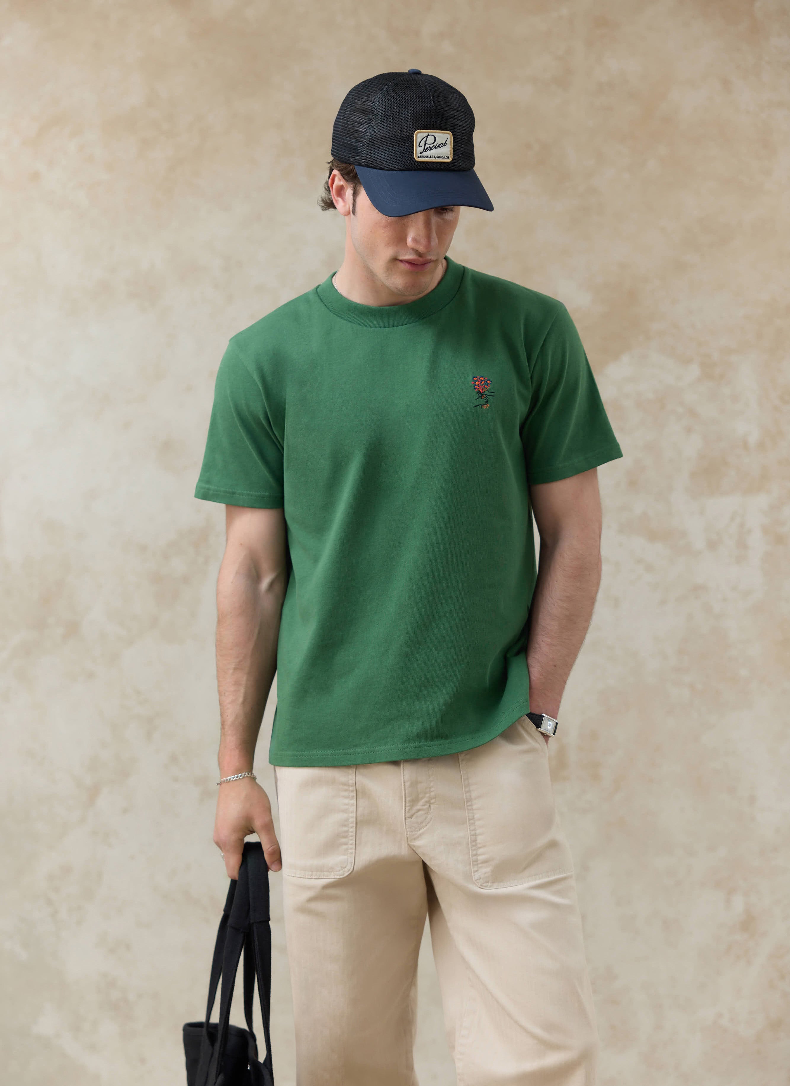 The Percival Davies Embroidered T Shirt in forest green organic cotton, styled with neutral trousers and a cap.