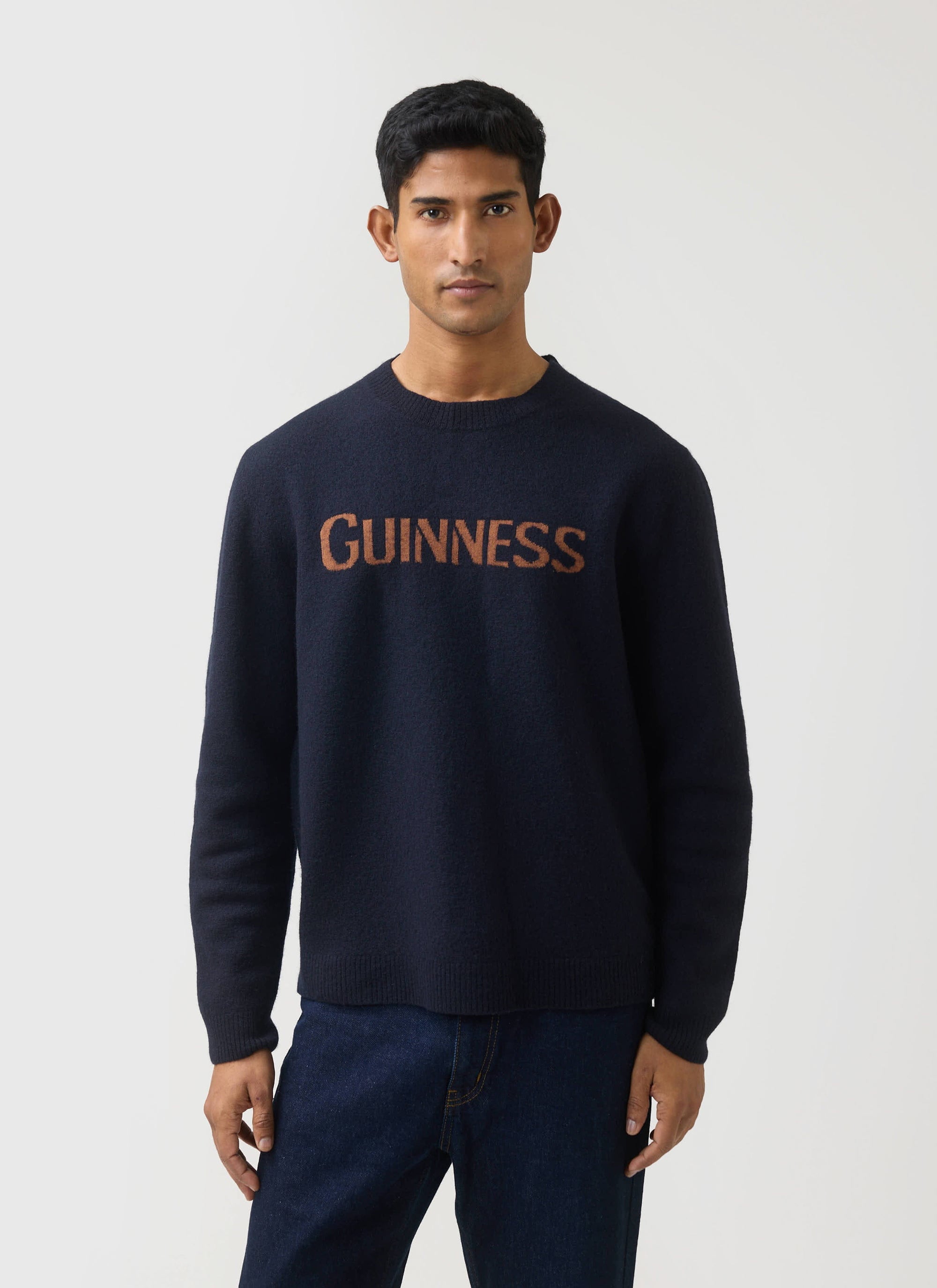 A man models the navy merino wool jumper from the Guinness x Percival collection, featuring the jacquard Guinness logo.