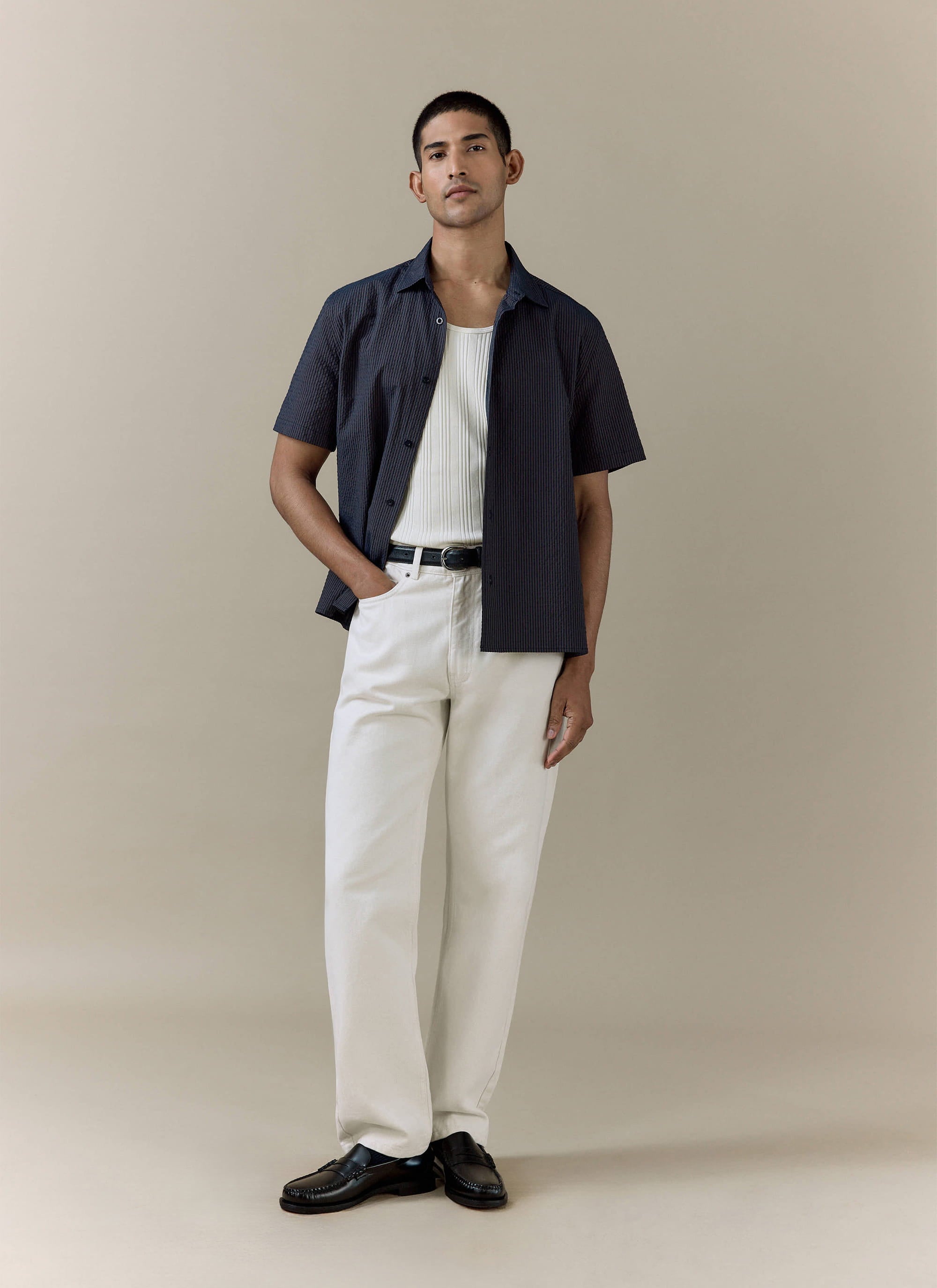 Model wears a Percival navy stripe Rowan Seersucker Boxy Shirt and cream straight leg denim jeans.