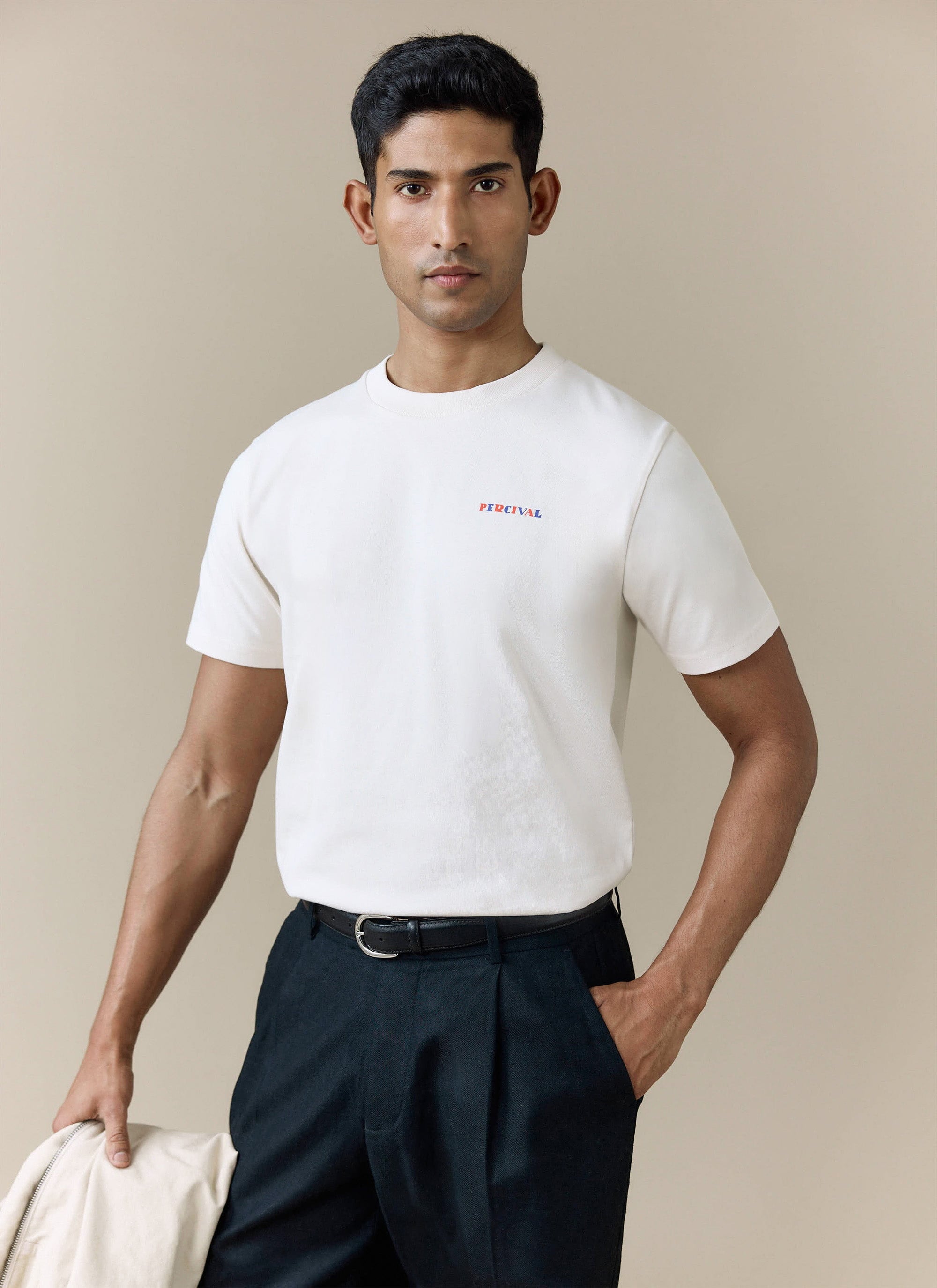 A model wears the ecru organic cotton Mixologist Martini T Shirt from Percival, styled with smart dark trousers.