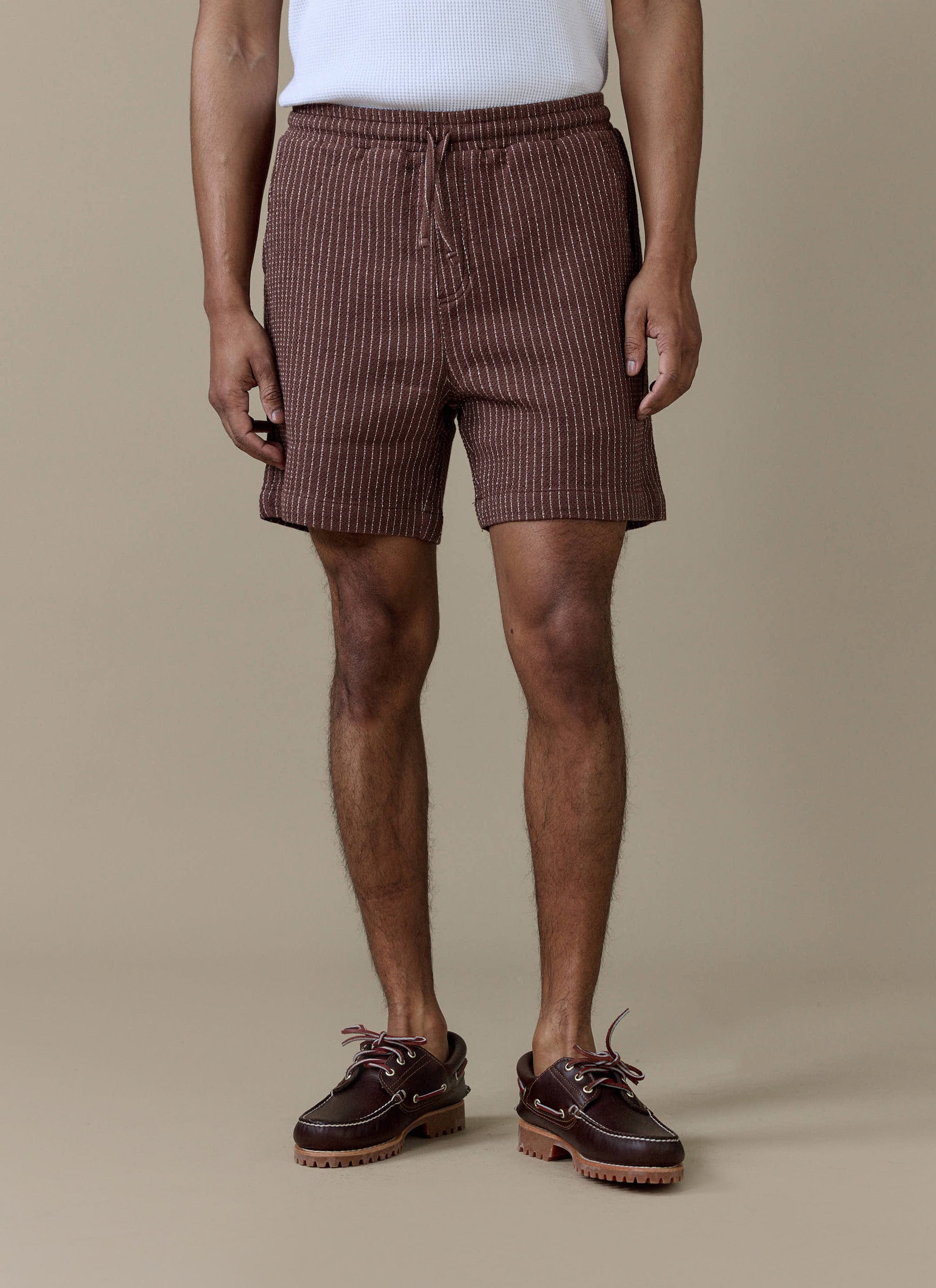 A model wearing the Percival Sorrento Shorts in brown linen, featuring a subtle vertical stripe and drawstring waistband.