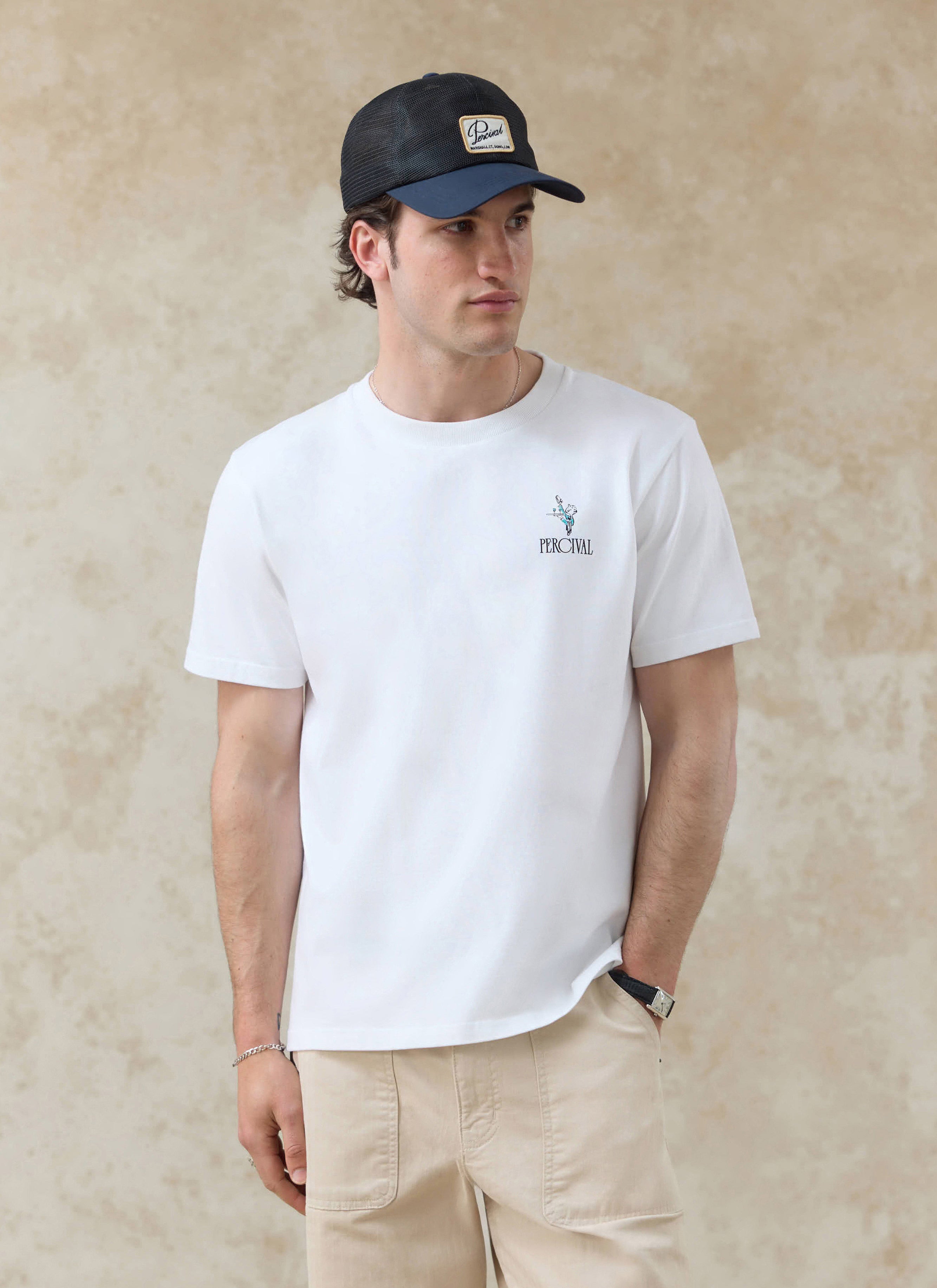 White organic cotton Percival Walker T-shirt with a small chest graphic, styled on a model with a mesh cap.