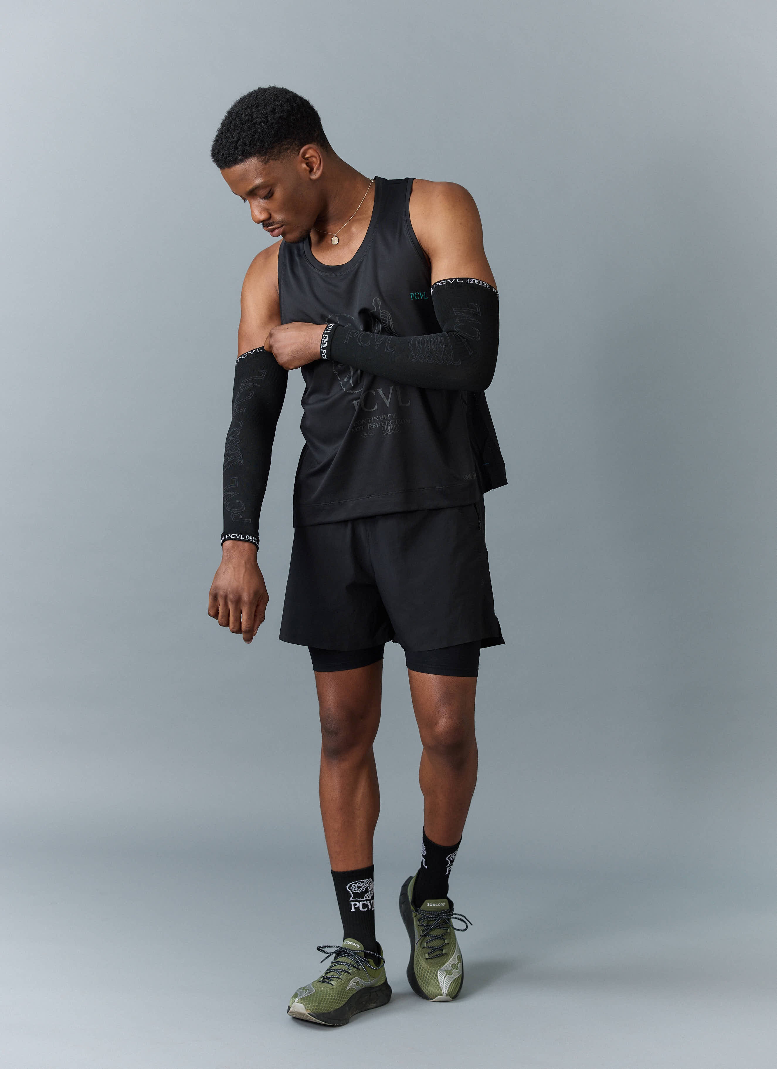 A model adjusts the black PCVL Arm Compression sleeve from Percival, styled with a full black athletic training kit.