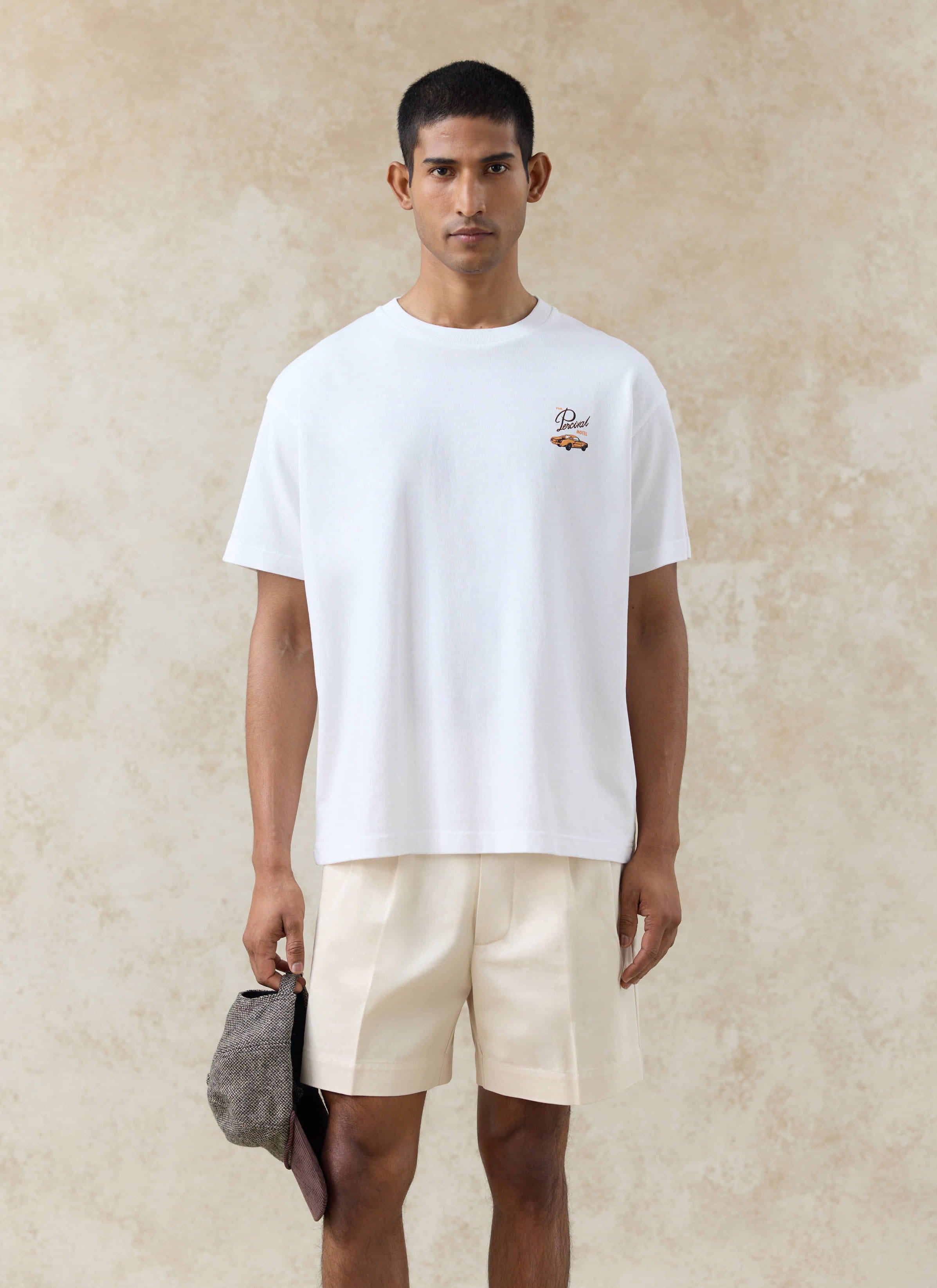 White Alistair oversized organic cotton t-shirt by Percival, featuring a car chest graphic and cream pleated shorts.