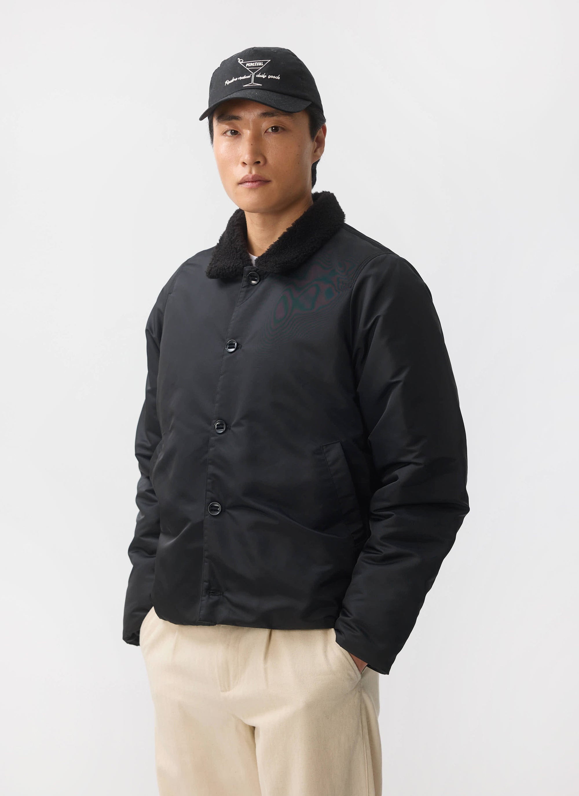 A man models the black Percival Doppio Bomber Jacket with its shearling collar against a white studio background.