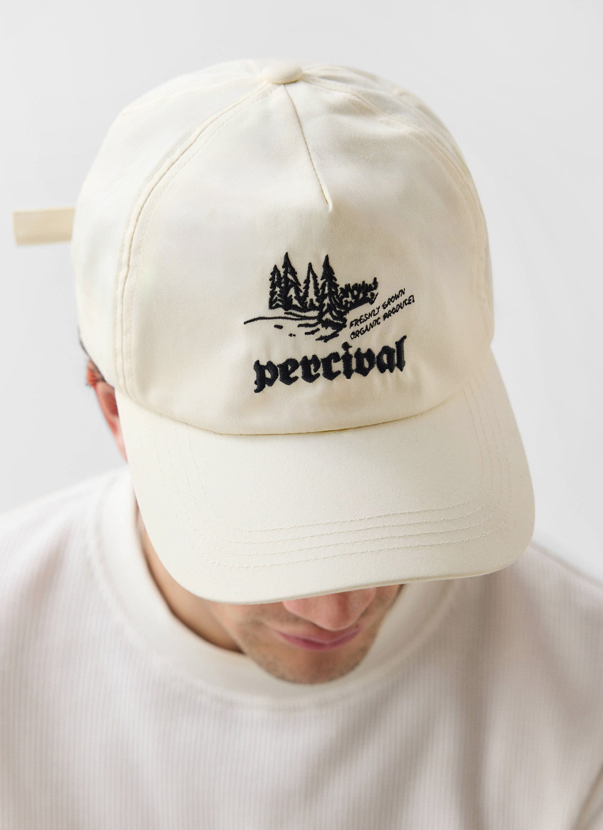 A close-up of a model wearing the ecru Wildlands Soft Trucker Cap, showing off the detailed Percival embroidery.