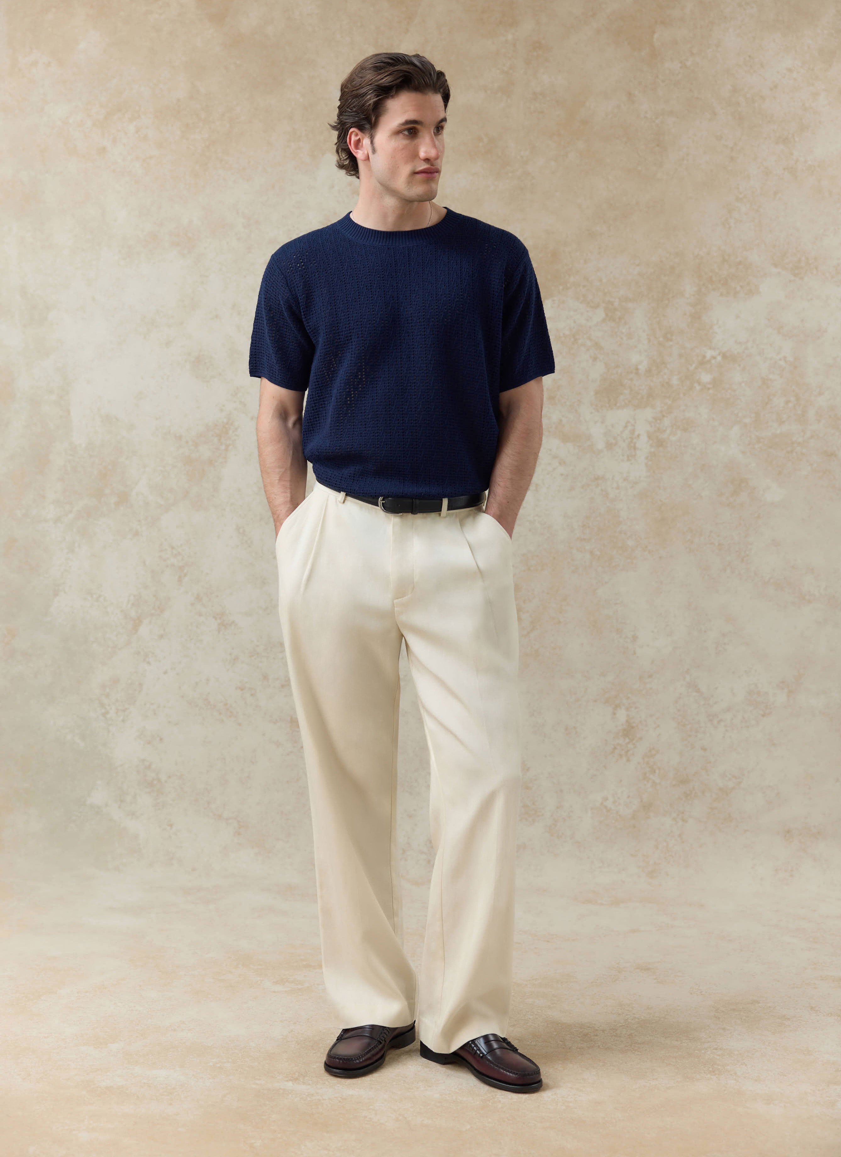 The Percival Siena Knitted T Shirt in navy, a textured cotton knit styled with cream pleated trousers and loafers.