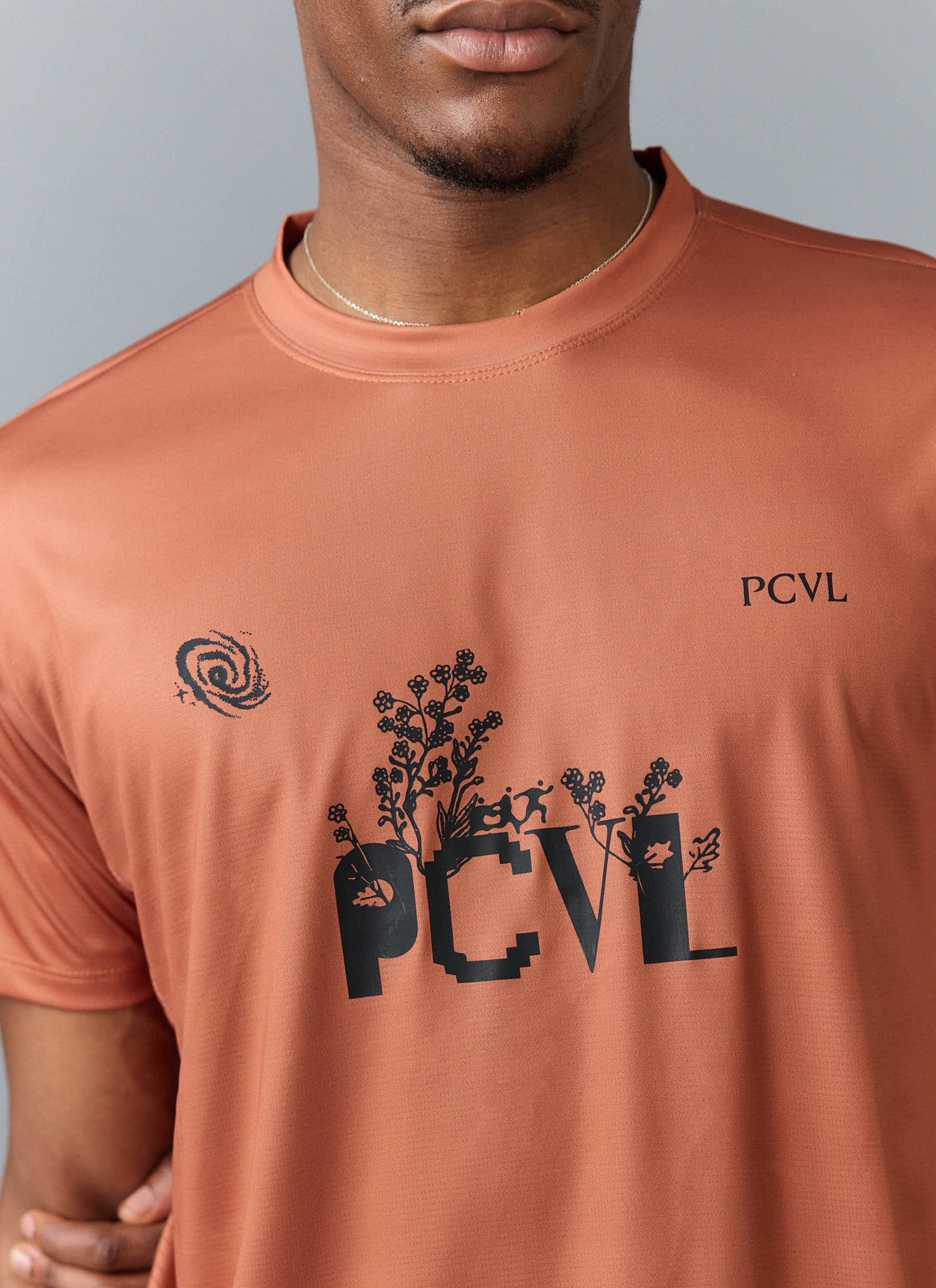 Close up of a model wearing the Percival PCVL Printed Performance Top in rust, showing the black graphic on the chest.