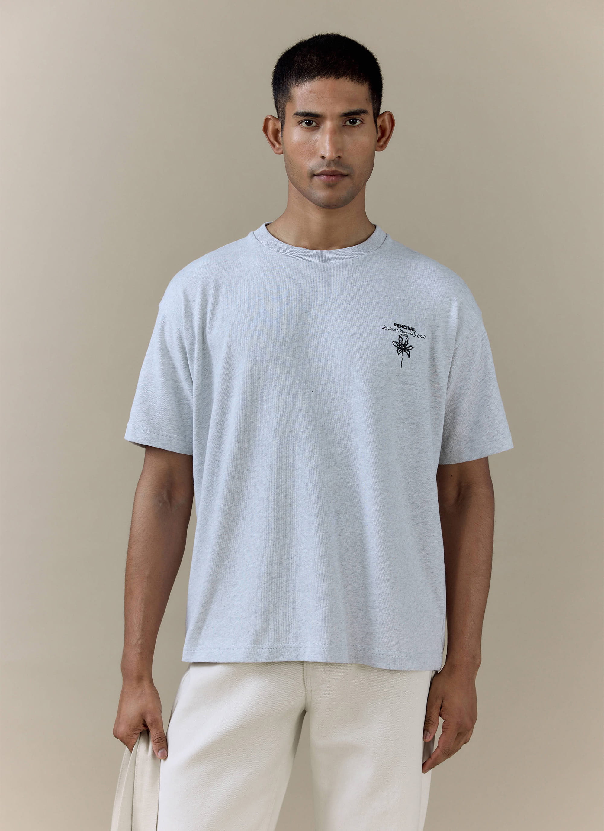 A model wearing the Percival Melvin Oversized T Shirt in grey organic cotton, featuring a black floral chest graphic.