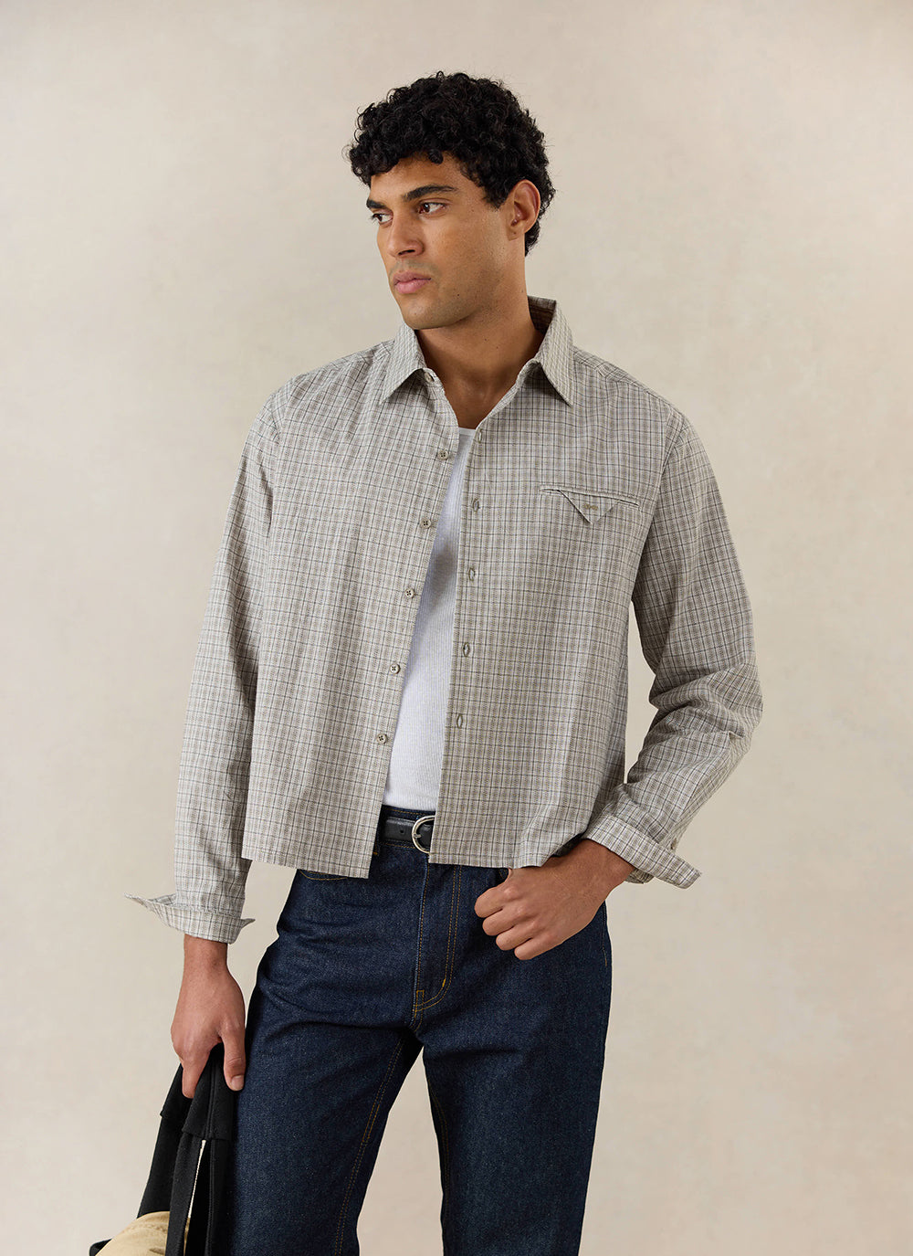 A model wears the cream Percival Hinsley Boxy Long Sleeve Shirt in cotton check, styled with dark jeans and a vest.