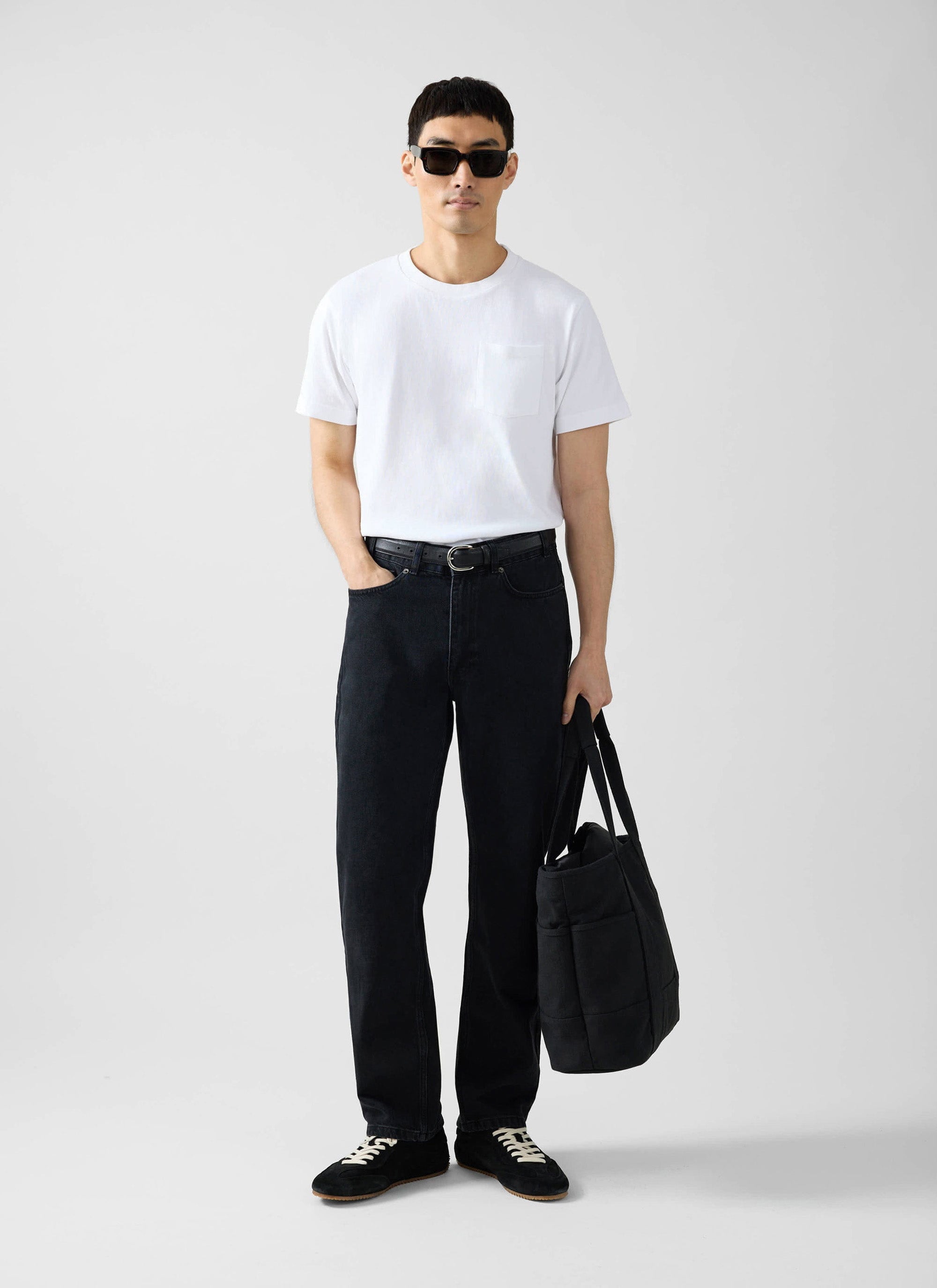 A model wears the Percival white organic cotton pocket t-shirt, styled with black jeans, sunglasses and a black tote bag.