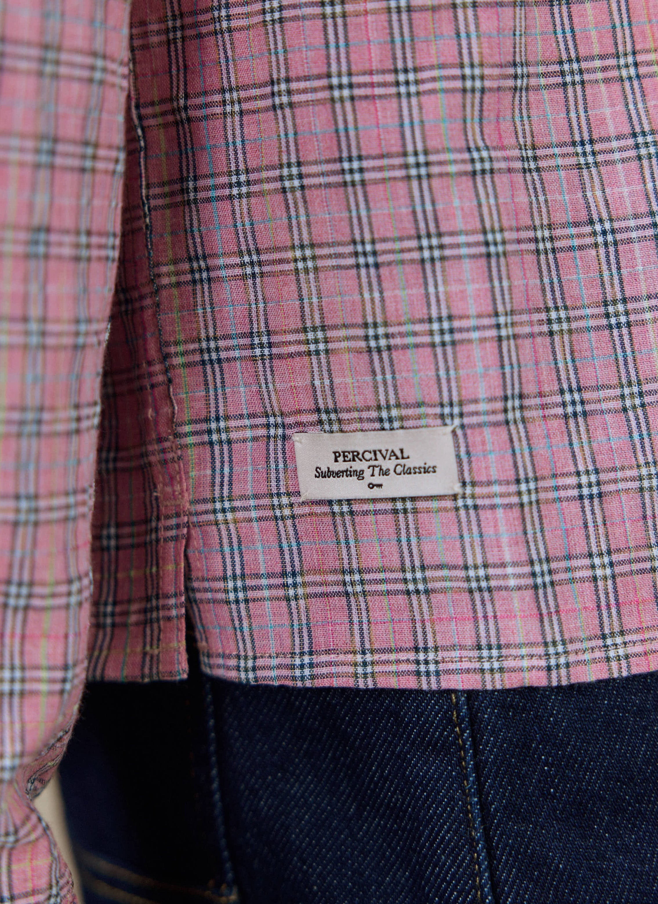 A close-up of the pink check fabric and woven brand tag on the Percival Hinsley Checked Boxy Shirt.
