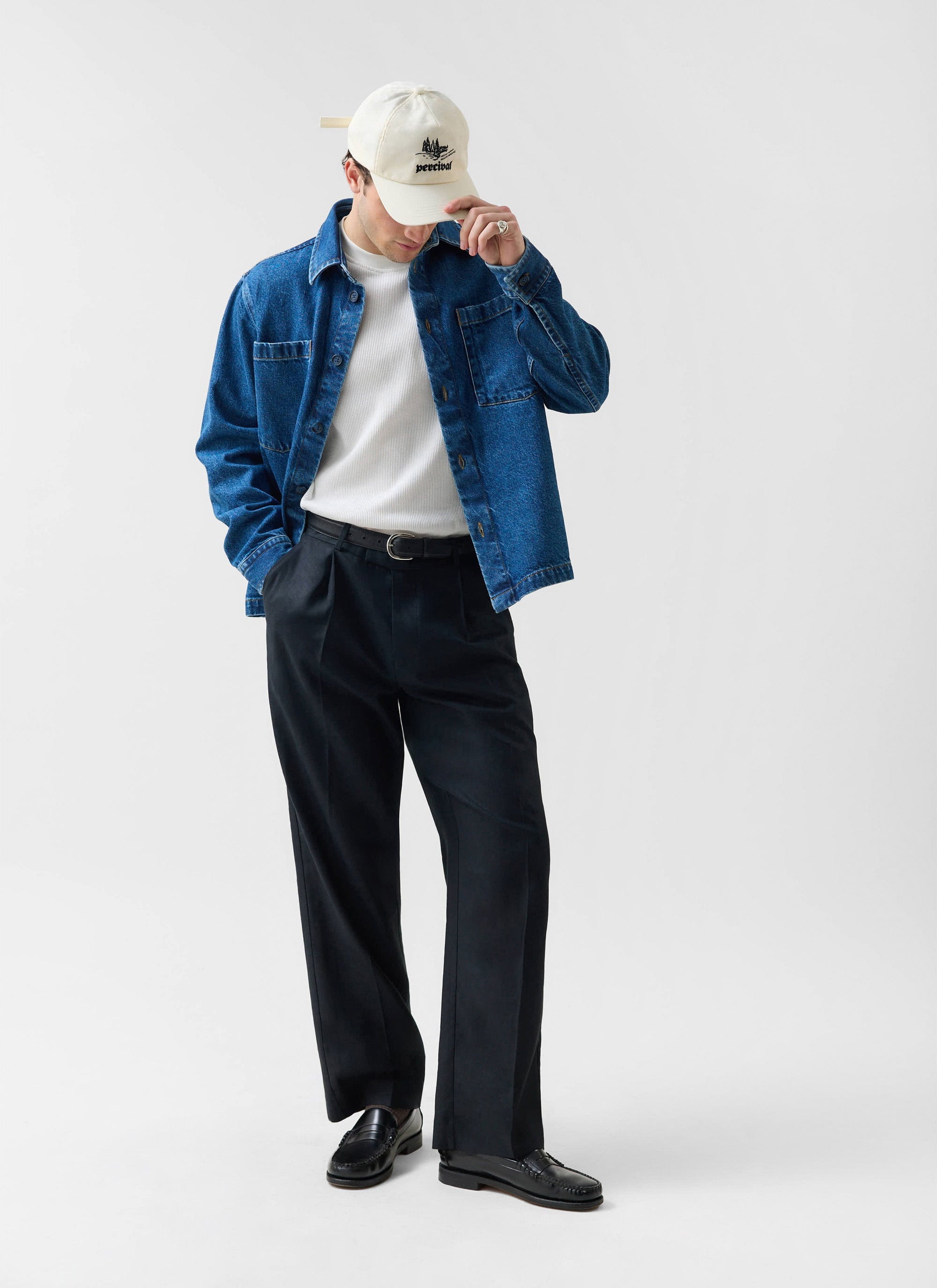 A man models the Percival Denim Heavyweight Overshirt in mid-wash blue with black trousers and a white t-shirt.