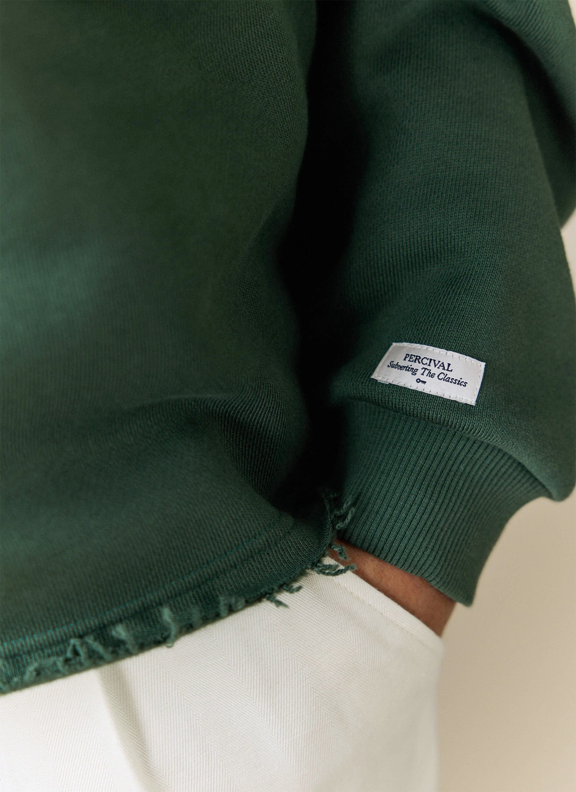 A close-up on the sleeve of the Percival Dudley Boxy Sweatshirt, showing the 'Subverting The Classics' brand label.