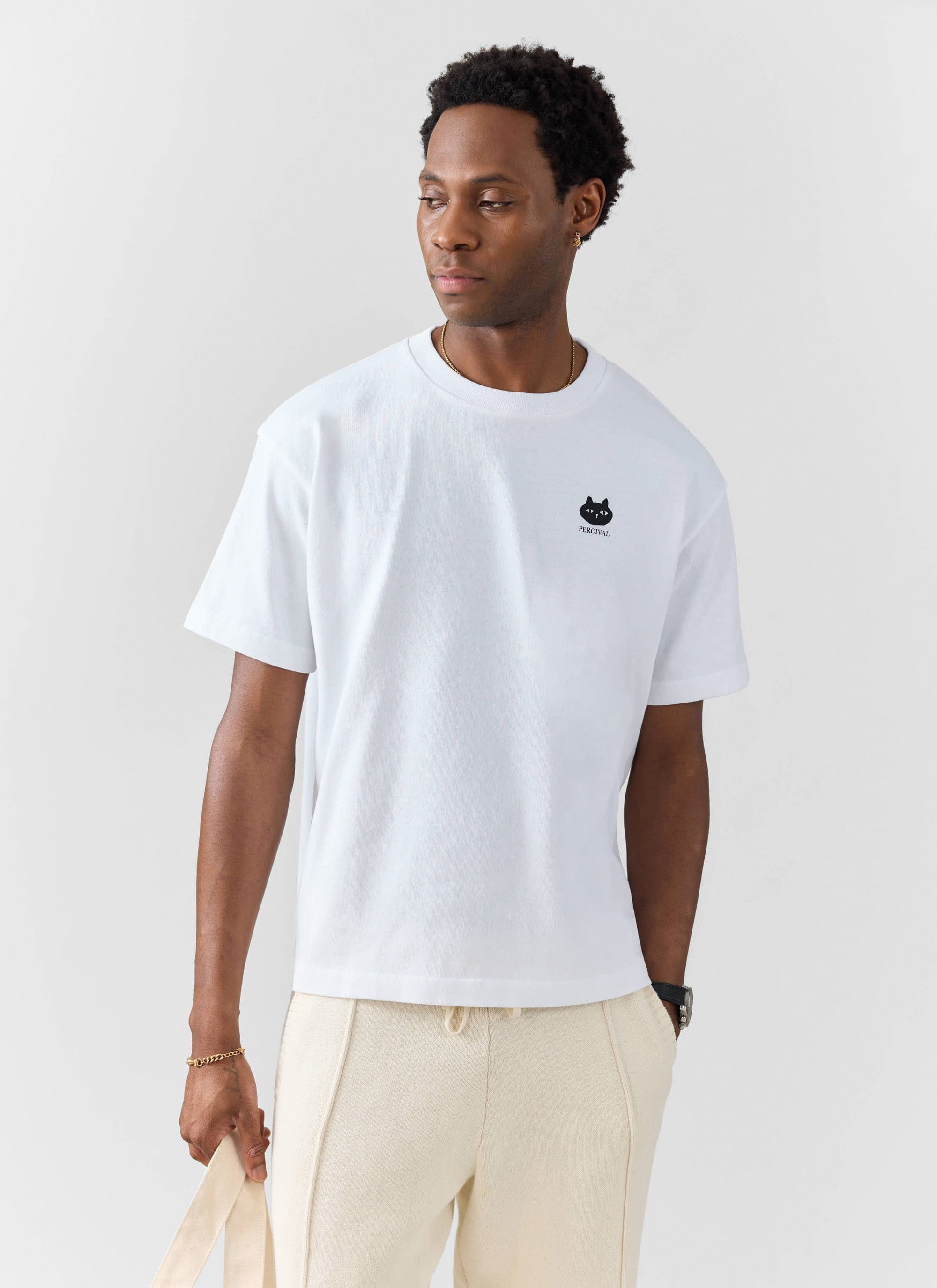 A man models the Percival Perci Loaf oversized t-shirt in white, paired with cream trousers against a white background.